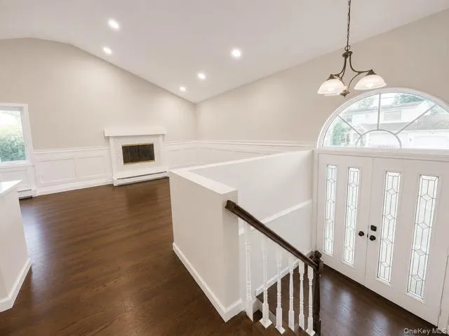 Elegant foyer showcasing gleaming wood-finish flooring, white wainscoting with chair rail detail, a curved staircase with dark wood handrail, recessed ceiling lighting, and a grand arched transom window with multi-pane glazing flanking the entry doors Elegant foyer showcasing gleaming wood-finish flooring, white wainscoting with chair rail detail, a curved staircase with dark wood handrail, recessed ceiling lighting, and a grand arched transom window with multi-pane glazing flanking the entry doors