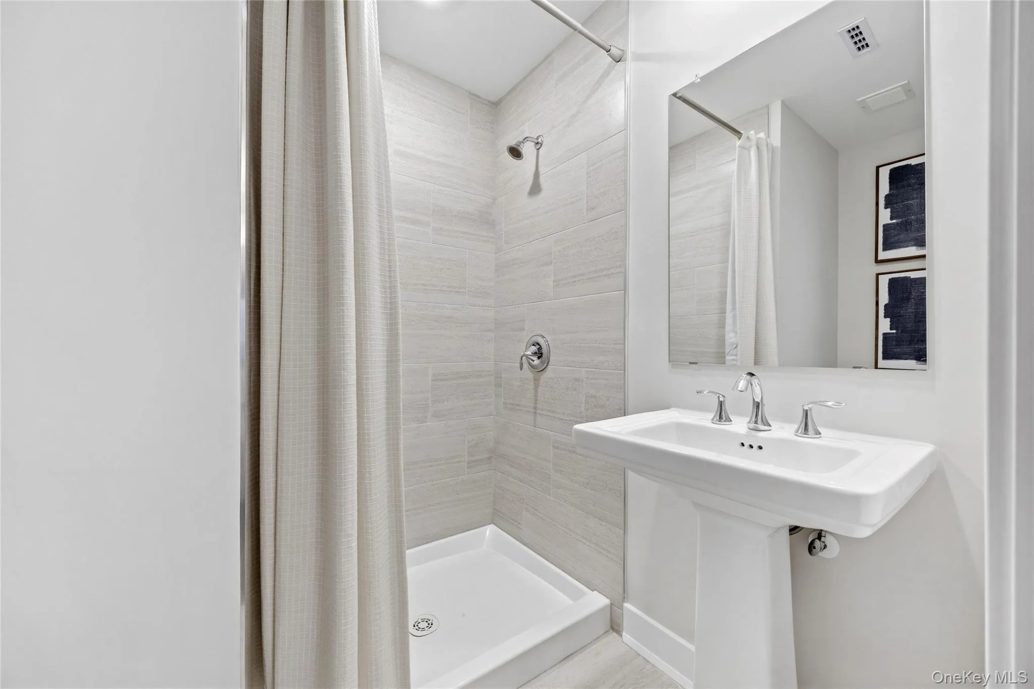 Basement Full Bathroom. Pedestal sink with chrome fixtures, a framed mirror, and a shower with light-toned wall tile Basement Full Bathroom. Pedestal sink with chrome fixtures, a framed mirror, and a shower with light-toned wall tile