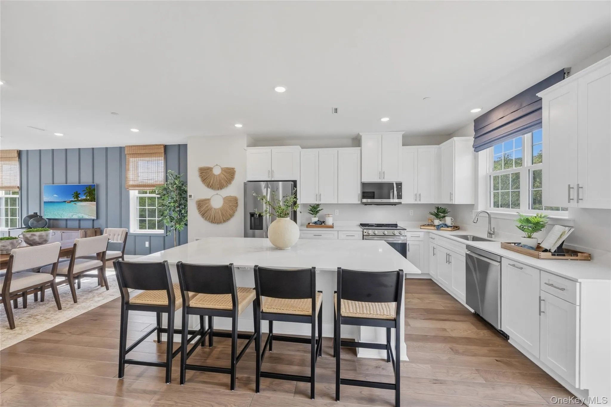 Open-concept kitchen featuring an spacious island with seating, white shaker cabinetry, stainless steel appliances, and wood-finish flooring Open-concept kitchen featuring an spacious island with seating, white shaker cabinetry, stainless steel appliances, and wood-finish flooring