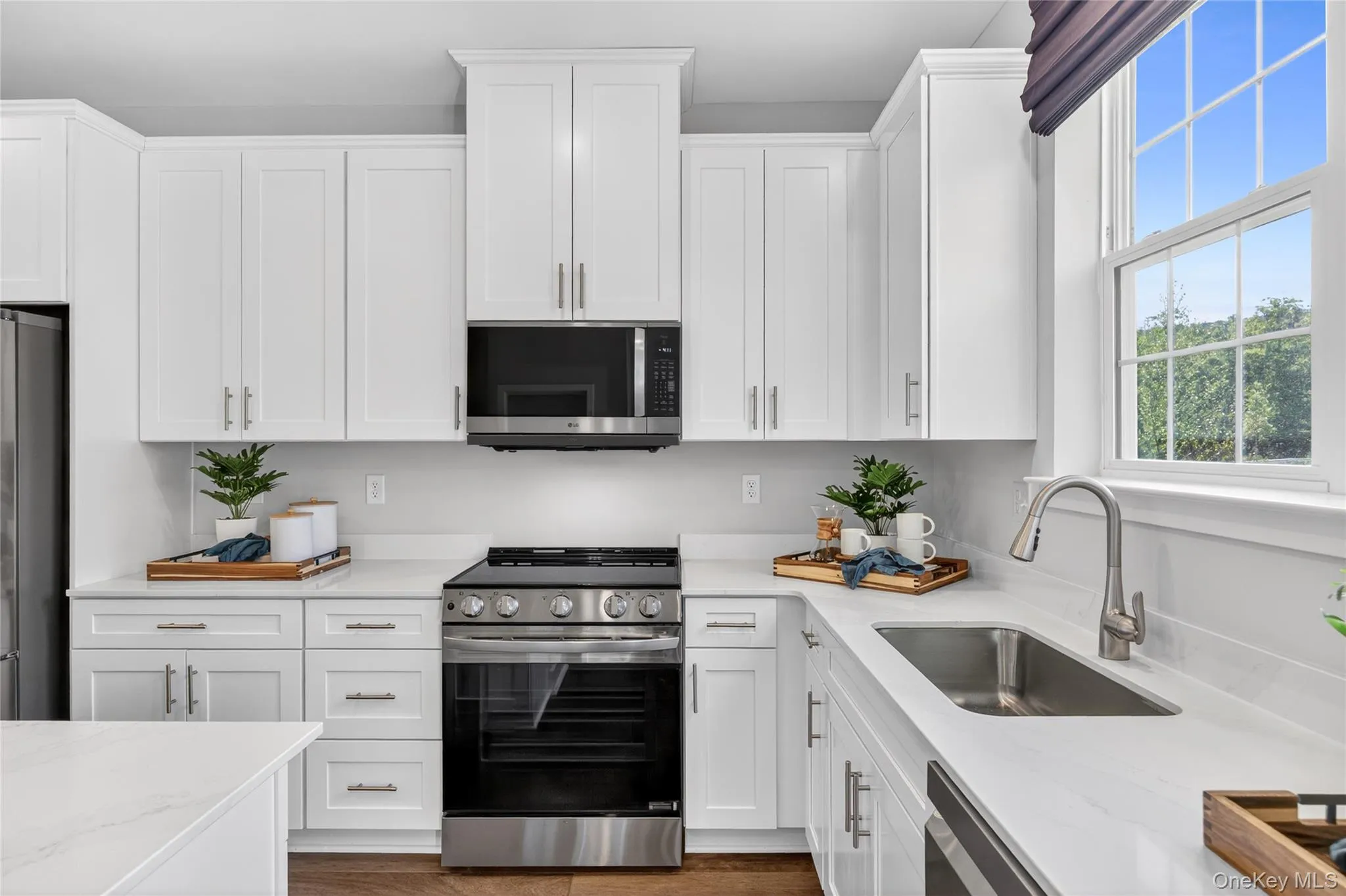 Modern kitchen featuring white shaker cabinetry, stainless steel appliances, light-toned countertops, and a stainless steel sink with a gooseneck faucet Modern kitchen featuring white shaker cabinetry, stainless steel appliances, light-toned countertops, and a stainless steel sink with a gooseneck faucet
