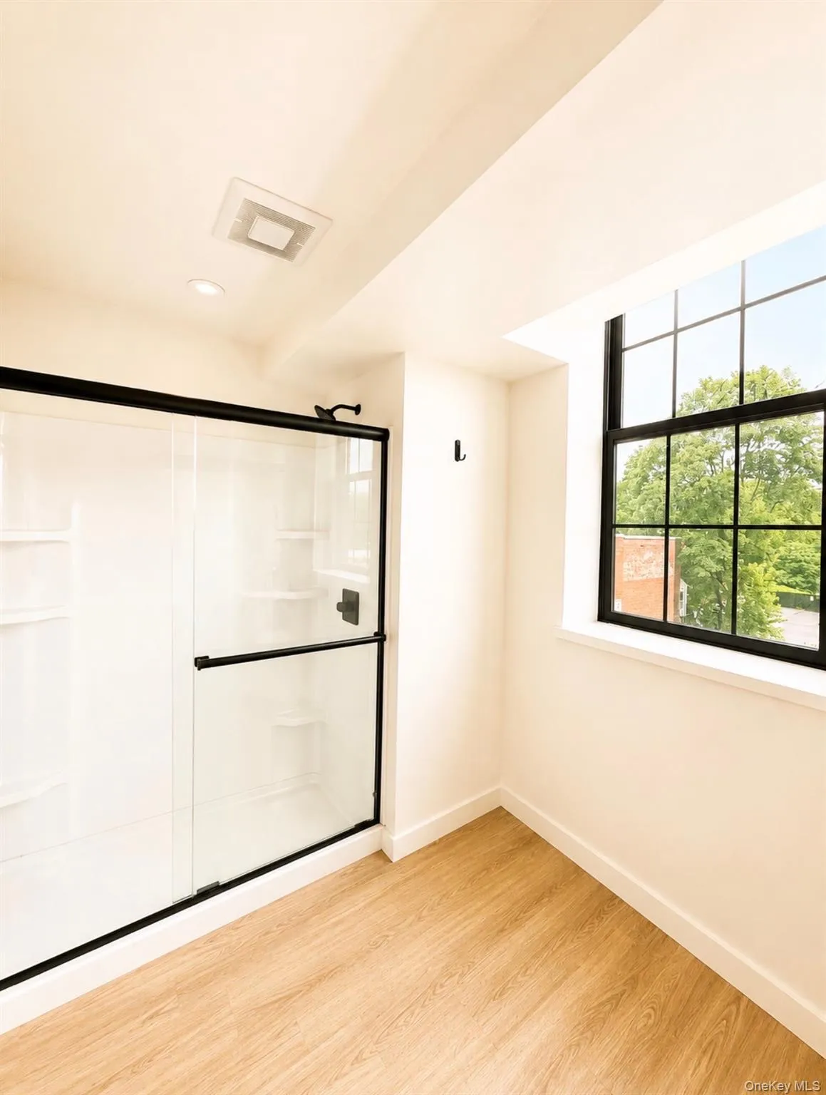 Walk-in shower with black-framed glass enclosure, wood-finish flooring, and a large multi-pane window Walk-in shower with black-framed glass enclosure, wood-finish flooring, and a large multi-pane window