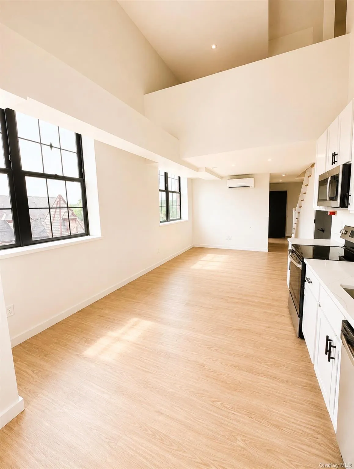 Spacious living area with wood-finish flooring and abundant natural light from multiple large windows Spacious living area with wood-finish flooring and abundant natural light from multiple large windows