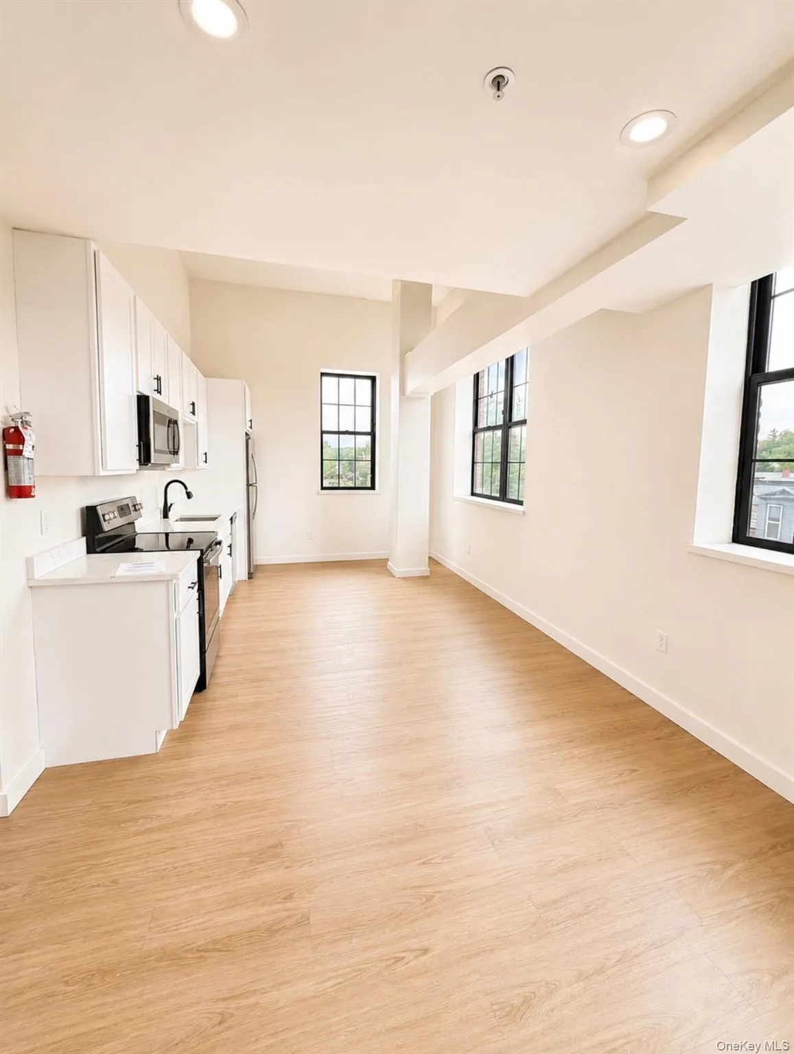 Open-concept living area featuring wood-finish flooring, white cabinetry, a built-in microwave, and large multi-pane windows Open-concept living area featuring wood-finish flooring, white cabinetry, a built-in microwave, and large multi-pane windows