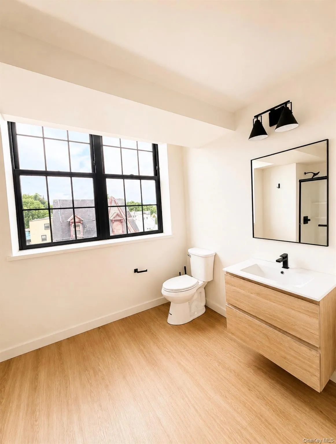 Large window with black grid panes, wood-finish flooring, floating wood-finish vanity with an integrated sink, matte black faucet, and a wall-mounted rectangular mirror Large window with black grid panes, wood-finish flooring, floating wood-finish vanity with an integrated sink, matte black faucet, and a wall-mounted rectangular mirror