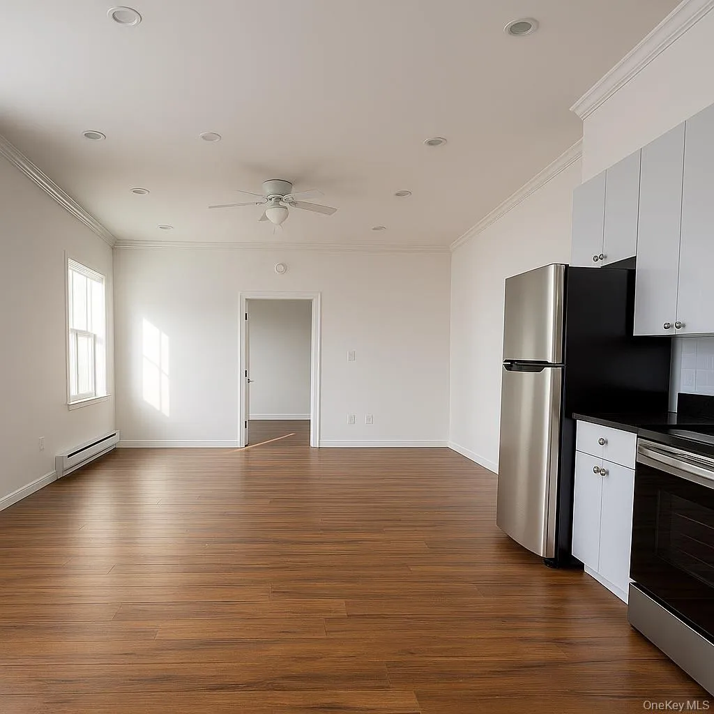 Kitchen with dark countertops, ornamental molding, appliances with stainless steel finishes, baseboard heating, and dark wood-type flooring Kitchen with dark countertops, ornamental molding, appliances with stainless steel finishes, baseboard heating, and dark wood-type flooring