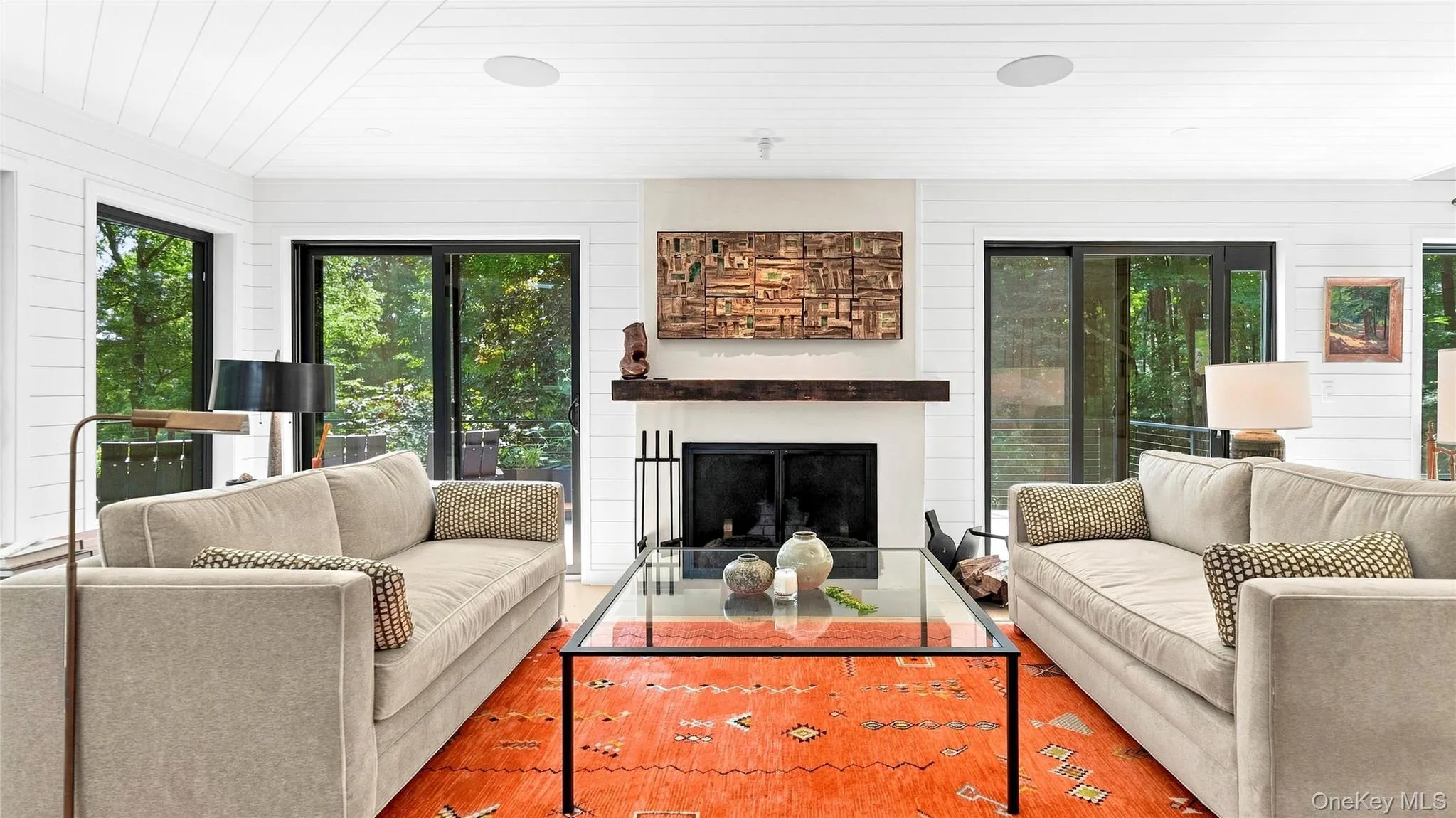 Light-filled living room with wood-burning fireplace, walls of glass and doors opening directly to the wraparound deck. Light-filled living room with wood-burning fireplace, walls of glass and doors opening directly to the wraparound deck.