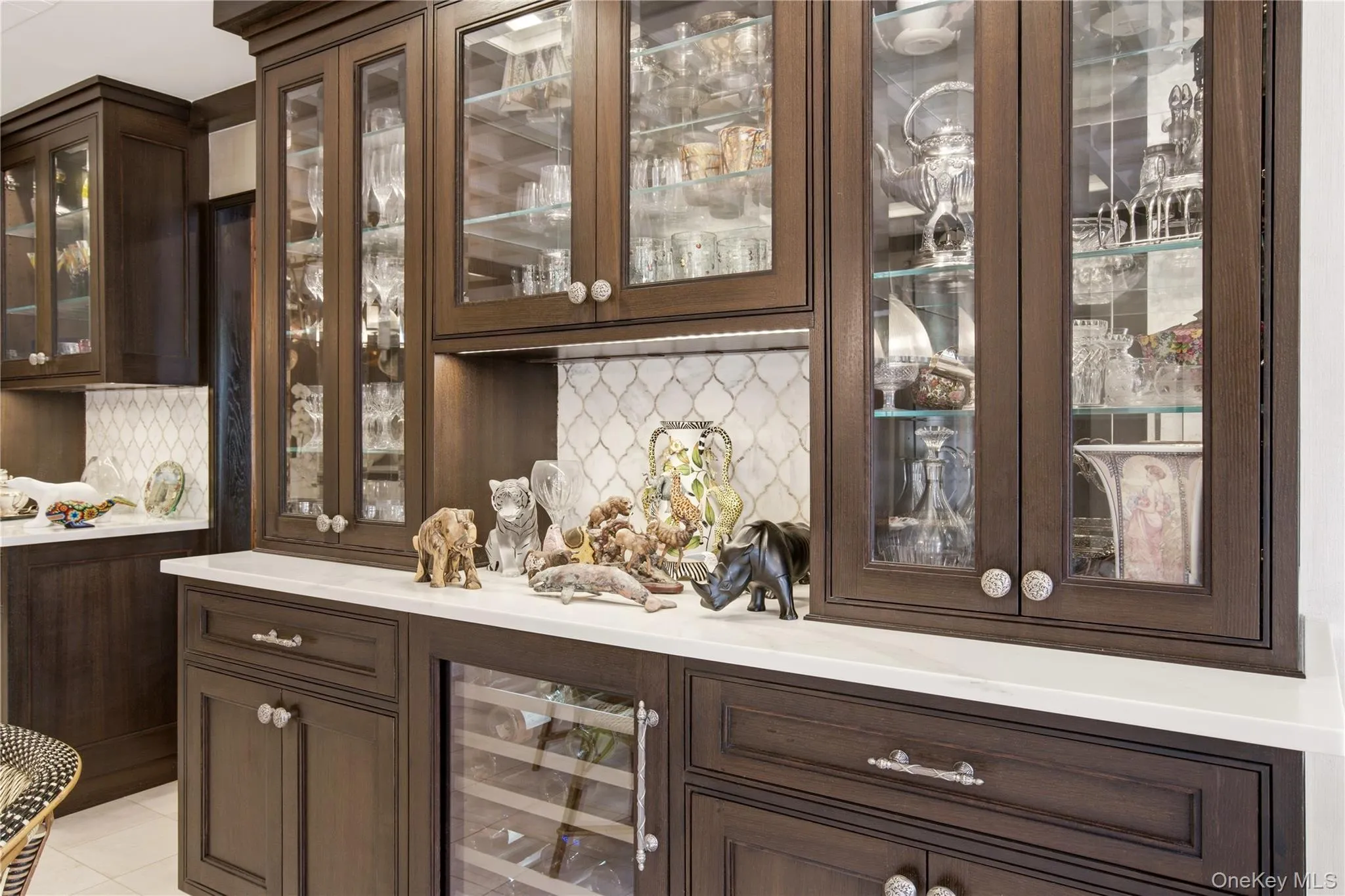 Built-in cabinetry with glass-front uppers, under-cabinet lighting, a patterned tile backsplash, and a beverage refrigerator Built-in cabinetry with glass-front uppers, under-cabinet lighting, a patterned tile backsplash, and a beverage refrigerator