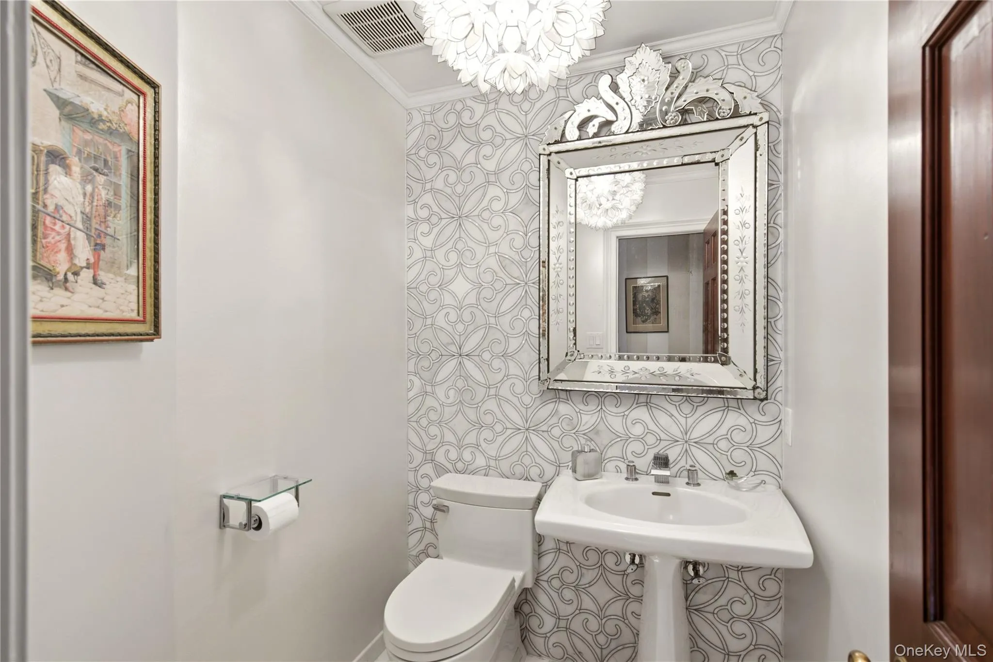Pedestal sink with chrome fixtures, decorative wall-mounted mirror, patterned accent wall, and ceiling-mounted light fixture Pedestal sink with chrome fixtures, decorative wall-mounted mirror, patterned accent wall, and ceiling-mounted light fixture