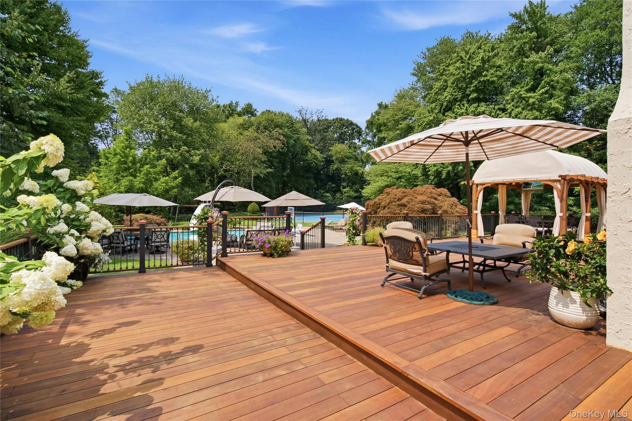 Multi-level wood deck with a built-in pergola ample seating areas, and a visible swimming pool surrounded by mature trees Multi-level wood deck with a built-in pergola ample seating areas, and a visible swimming pool surrounded by mature trees