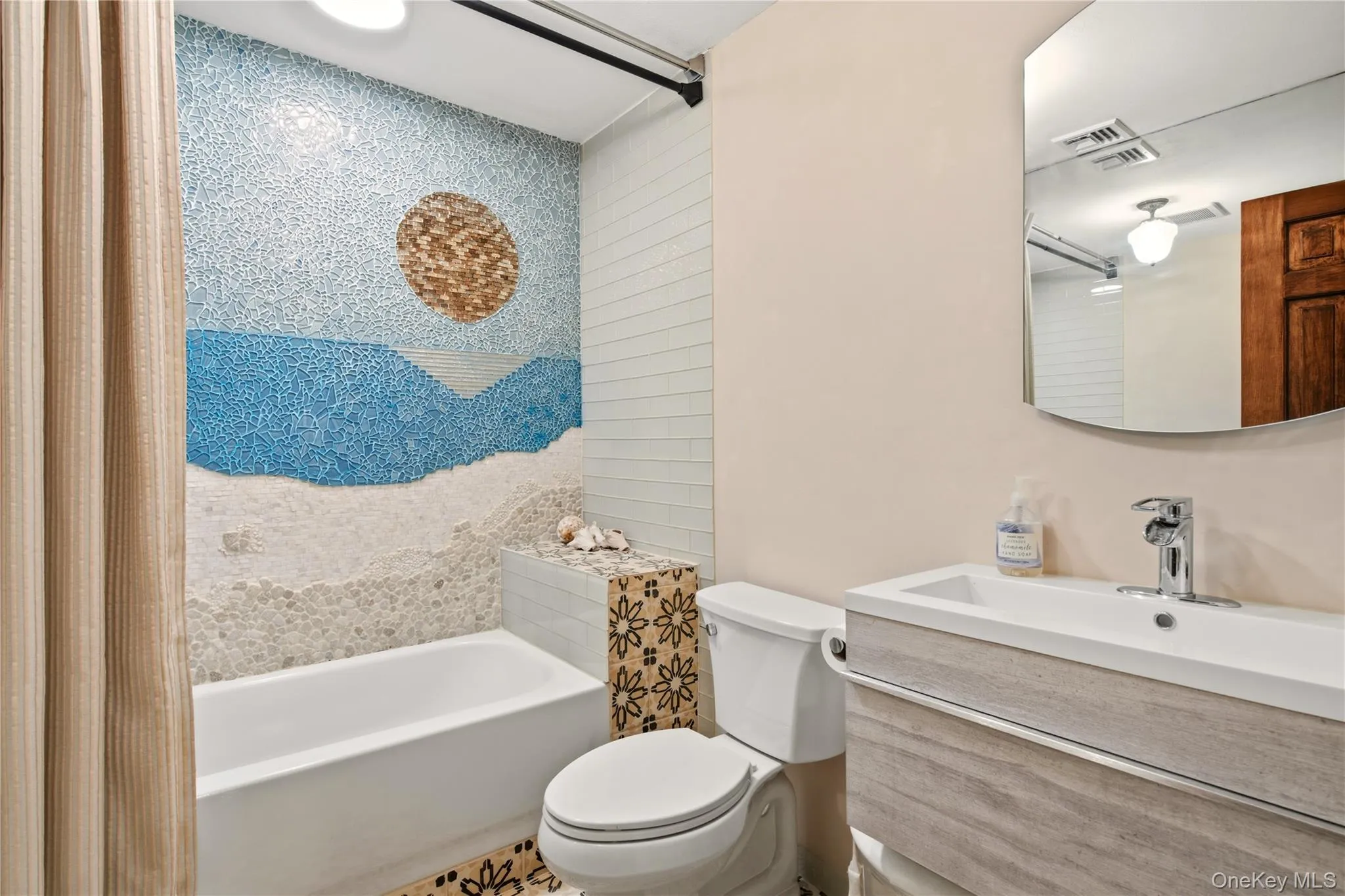 Bathtub with a mosaic-tiled accent wall, vanity with an integrated sink, and a wall-mounted mirror Bathtub with a mosaic-tiled accent wall, vanity with an integrated sink, and a wall-mounted mirror