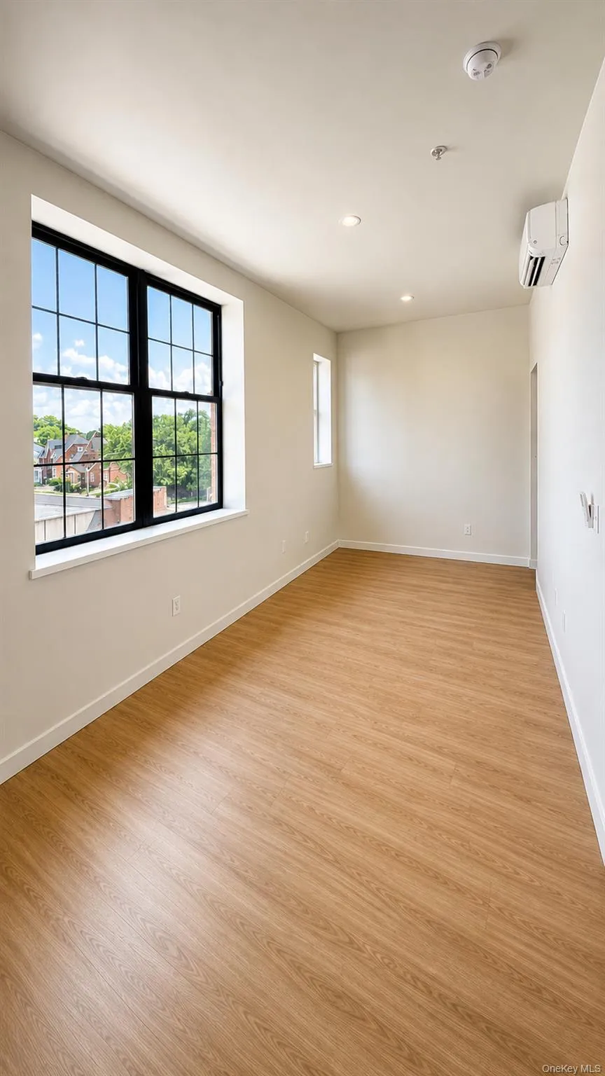 Wood-finish flooring throughout, large grid-pane window, recessed ceiling lighting, and a wall-mounted climate control unit Wood-finish flooring throughout, large grid-pane window, recessed ceiling lighting, and a wall-mounted climate control unit