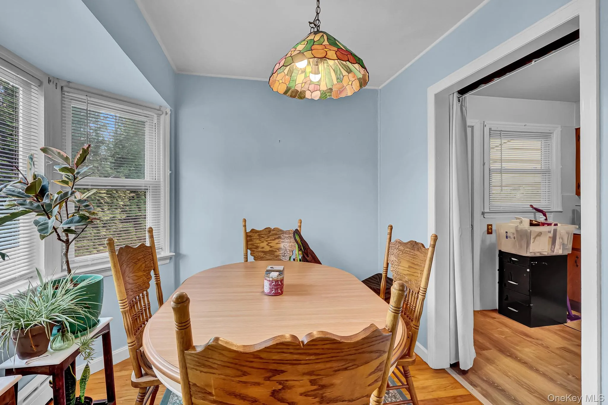 Bay window with white trim, wood-finish flooring, and a stained-glass pendant light fixture Bay window with white trim, wood-finish flooring, and a stained-glass pendant light fixture