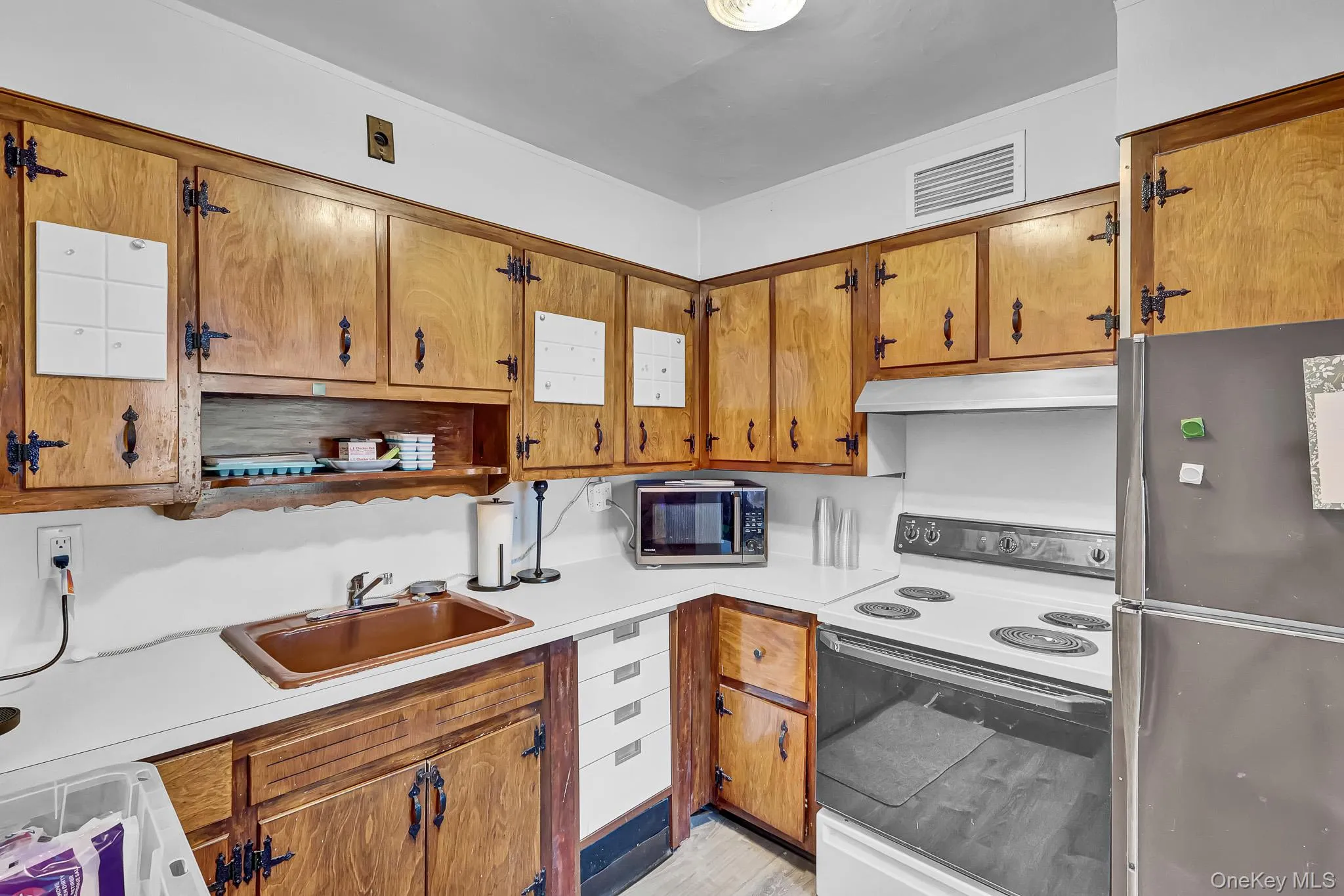 Wood cabinetry with decorative hardware, white countertops, built-in sink, electric range with exhaust hood, and refrigerator Wood cabinetry with decorative hardware, white countertops, built-in sink, electric range with exhaust hood, and refrigerator