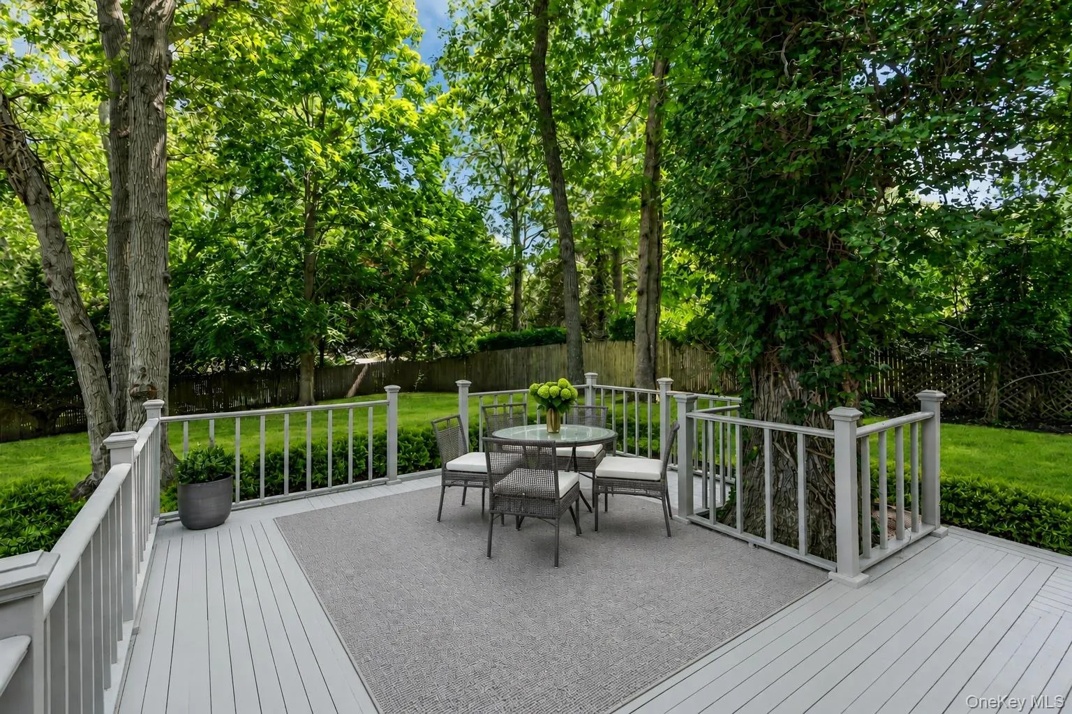Expansive outdoor deck with light gray decking and white railing, surrounded by mature trees and manicured lawn Expansive outdoor deck with light gray decking and white railing, surrounded by mature trees and manicured lawn