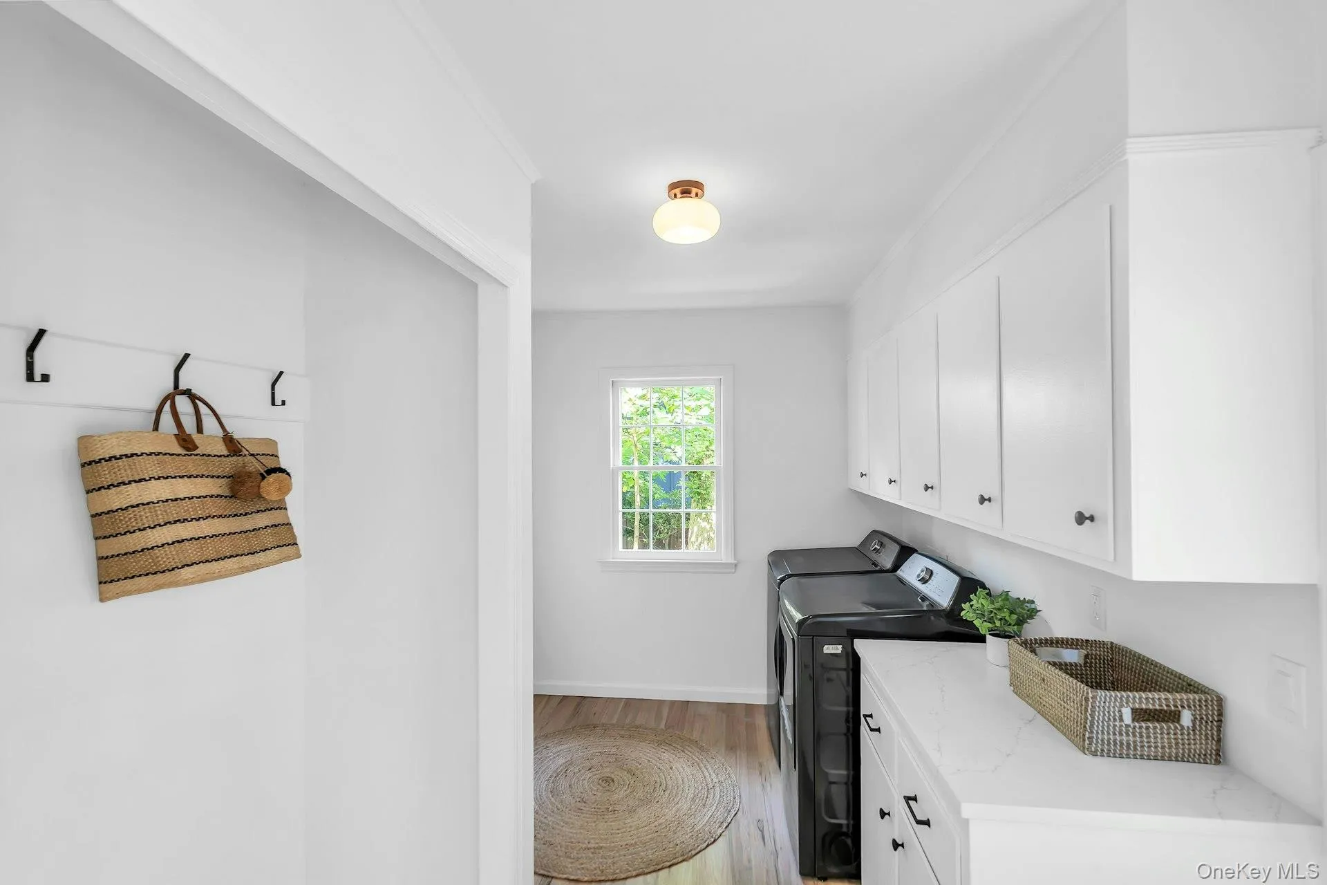 Laundry area featuring wood-finish flooring, white cabinetry, a built-in countertop, and a window Laundry area featuring wood-finish flooring, white cabinetry, a built-in countertop, and a window