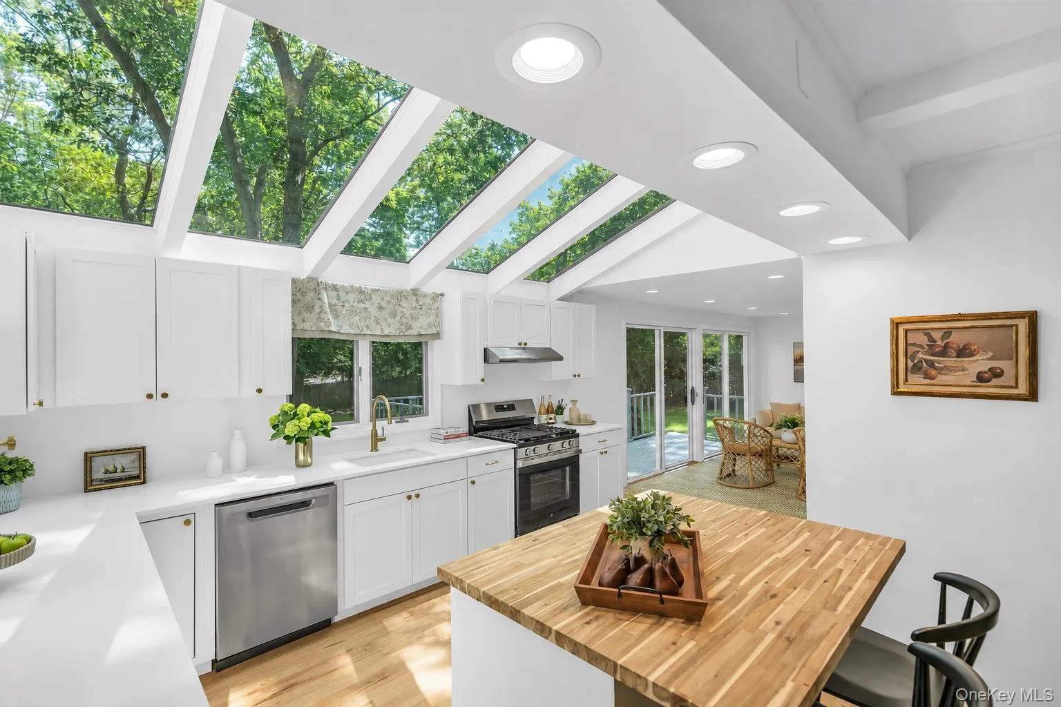 Kitchen with vaulted ceiling and integrated skylights, white cabinetry, stainless steel appliances, a wood-finish island, and recessed lighting Kitchen with vaulted ceiling and integrated skylights, white cabinetry, stainless steel appliances, a wood-finish island, and recessed lighting