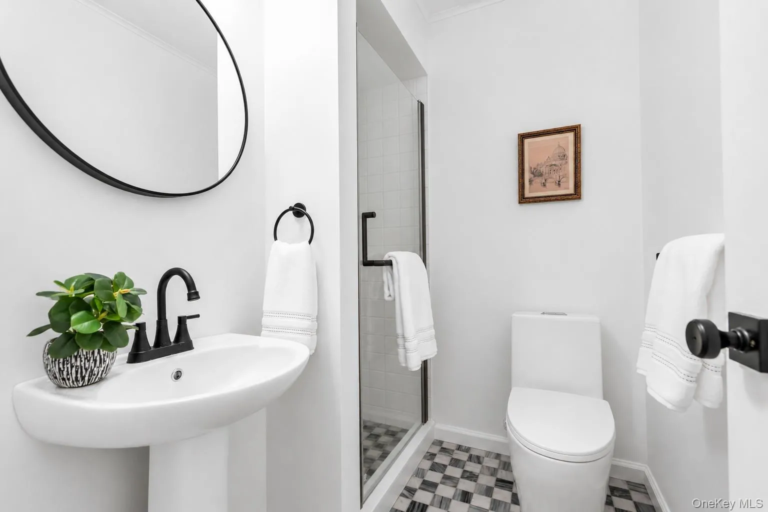 Pedestal sink with matte black faucet, checkered tile flooring, glass-enclosed shower, white toilet, and matte black door hardware Pedestal sink with matte black faucet, checkered tile flooring, glass-enclosed shower, white toilet, and matte black door hardware