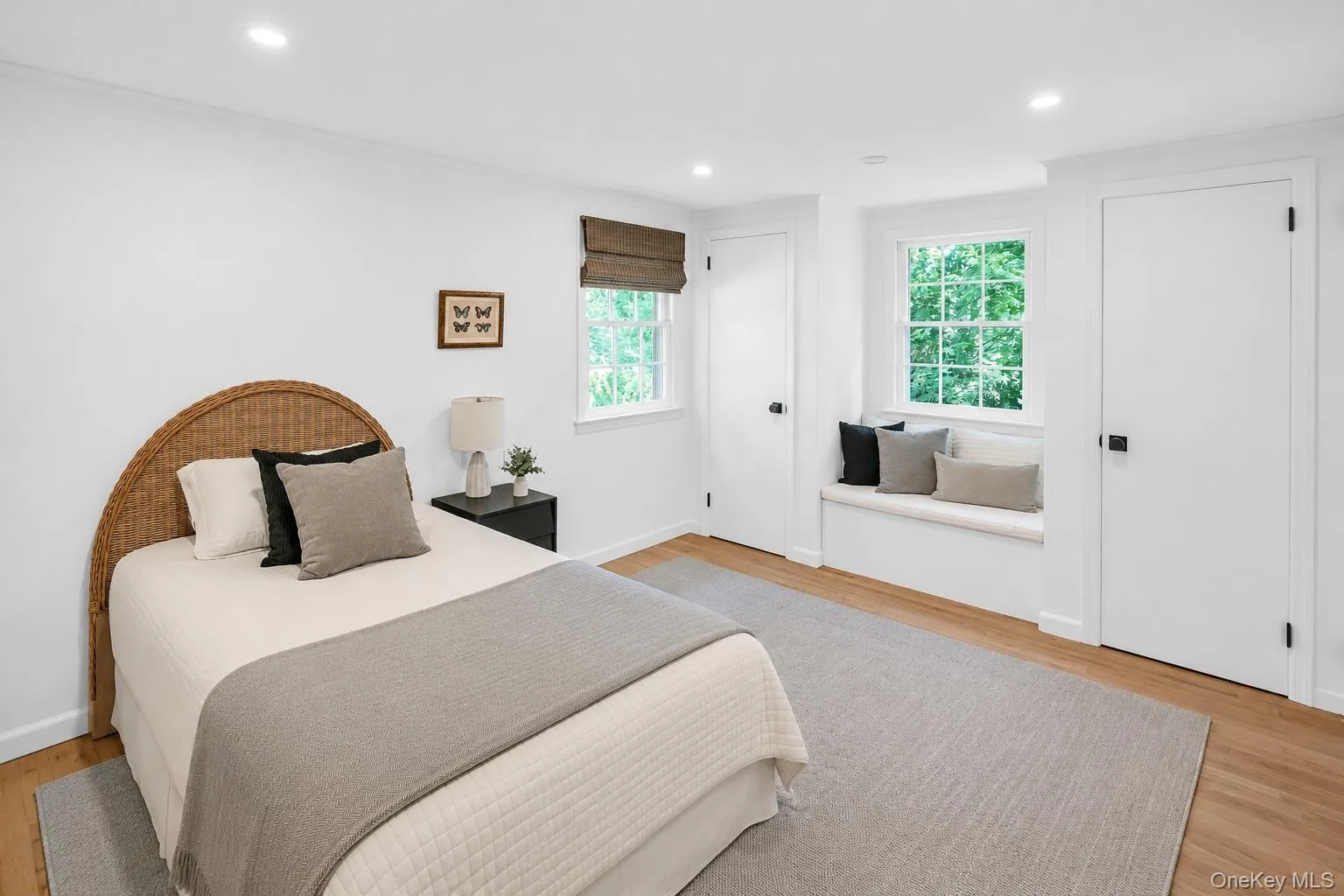 Recessed lighting, wood-finish flooring, two panel doors with black hardware, window with integrated seating, and a second window with a woven shade Recessed lighting, wood-finish flooring, two panel doors with black hardware, window with integrated seating, and a second window with a woven shade