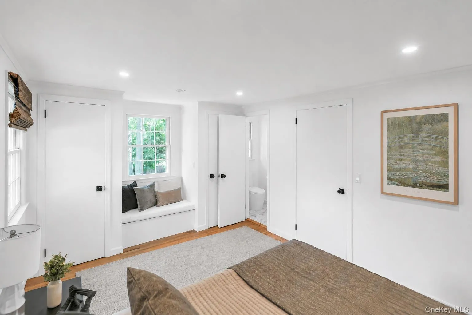 Window seat with integrated storage, wood-finish flooring, recessed lighting, white interior doors with dark hardware, and a window with natural light Window seat with integrated storage, wood-finish flooring, recessed lighting, white interior doors with dark hardware, and a window with natural light