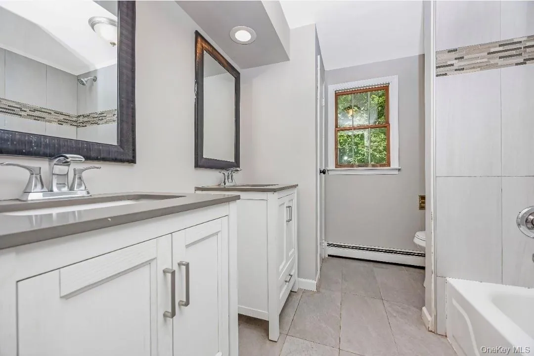 Dual vanities with integrated sinks and chrome fixtures, grey countertops, tiled flooring, and a tiled shower with a decorative mosaic accent Dual vanities with integrated sinks and chrome fixtures, grey countertops, tiled flooring, and a tiled shower with a decorative mosaic accent