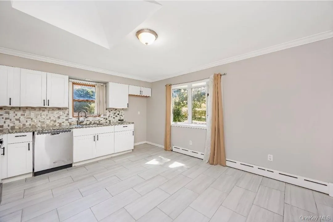 Kitchen featuring white shaker cabinetry, stainless steel dishwasher, mosaic tile backsplash, and light-toned tile flooring Kitchen featuring white shaker cabinetry, stainless steel dishwasher, mosaic tile backsplash, and light-toned tile flooring