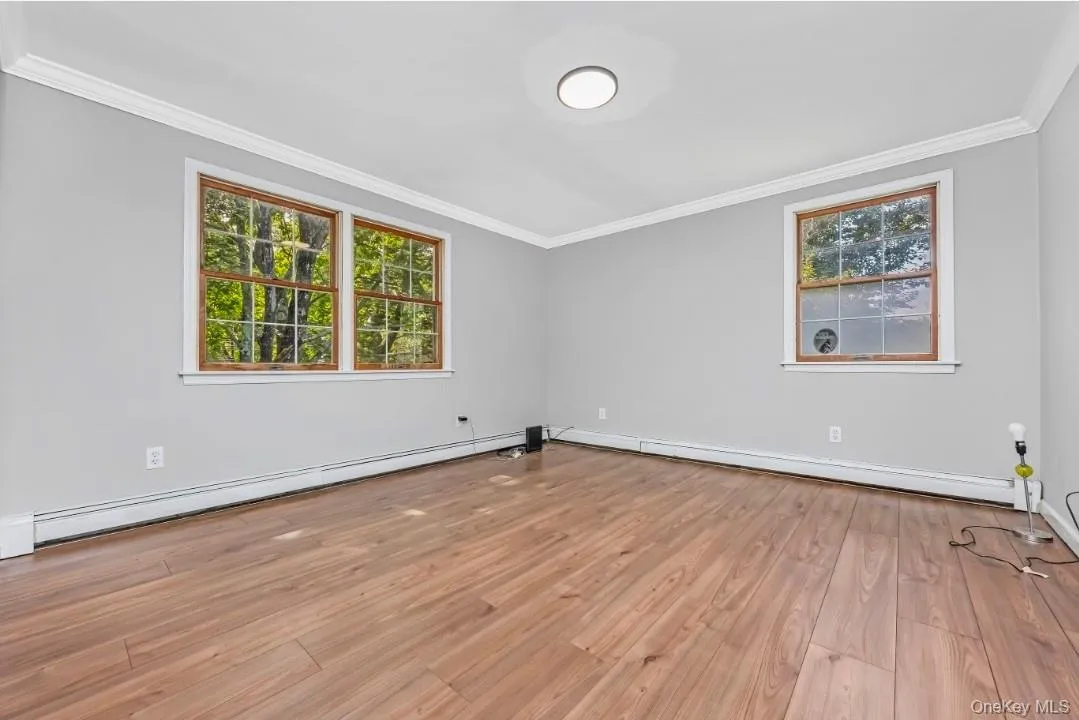Wood-finish flooring, light gray wall paint, white crown molding, and two windows with wood trim Wood-finish flooring, light gray wall paint, white crown molding, and two windows with wood trim