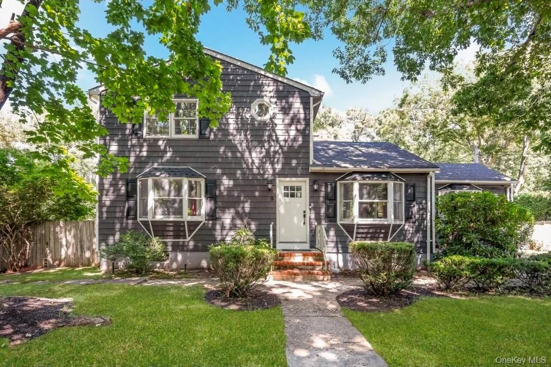 Dark gray shingle siding, white entry door with window pane detailing, two bay windows, round accent window, and a stone pathway leading to the entry Dark gray shingle siding, white entry door with window pane detailing, two bay windows, round accent window, and a stone pathway leading to the entry
