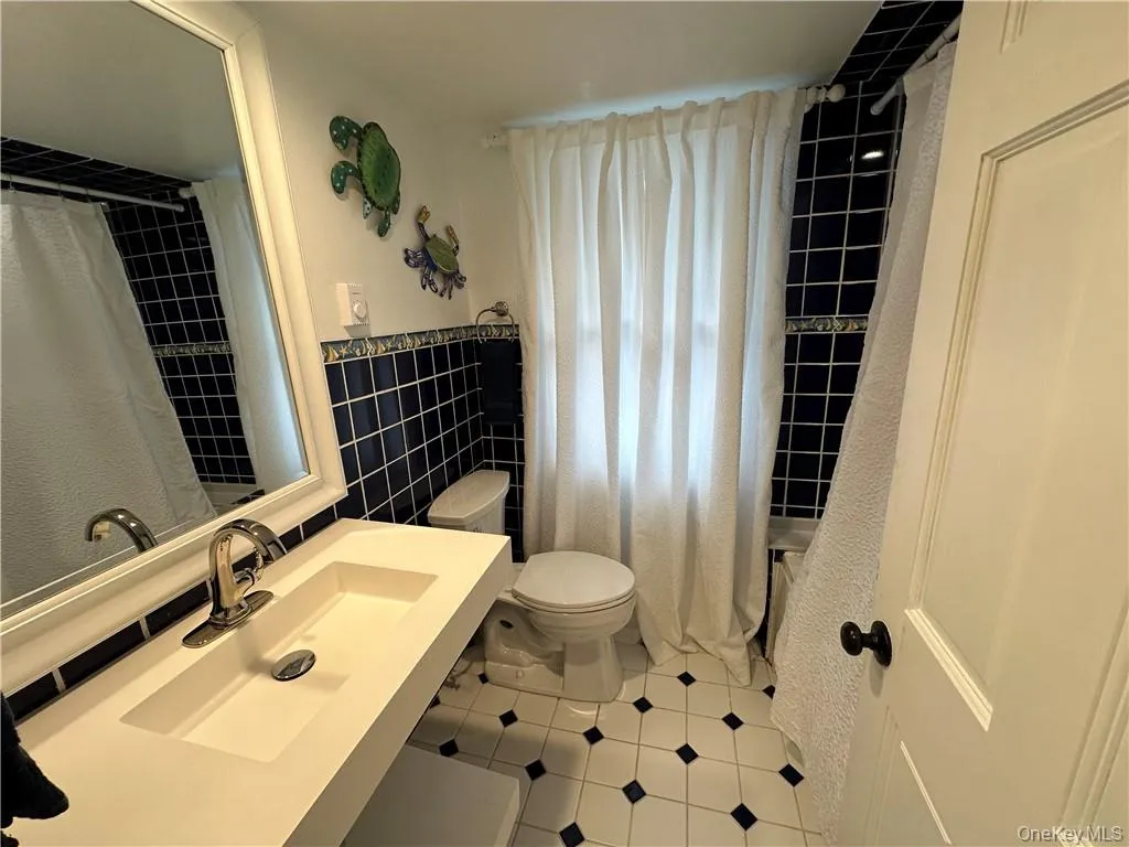 Full bathroom with tile walls, sink, toilet, and shower / tub combo Full bathroom with tile walls, sink, toilet, and shower / tub combo