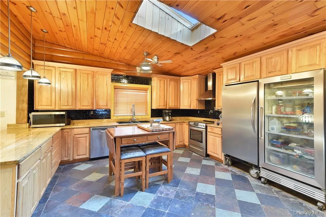 Kitchen with appliances with stainless steel finishes, a skylight, backsplash, hanging light fixtures, and light stone counters Kitchen with appliances with stainless steel finishes, a skylight, backsplash, hanging light fixtures, and light stone counters