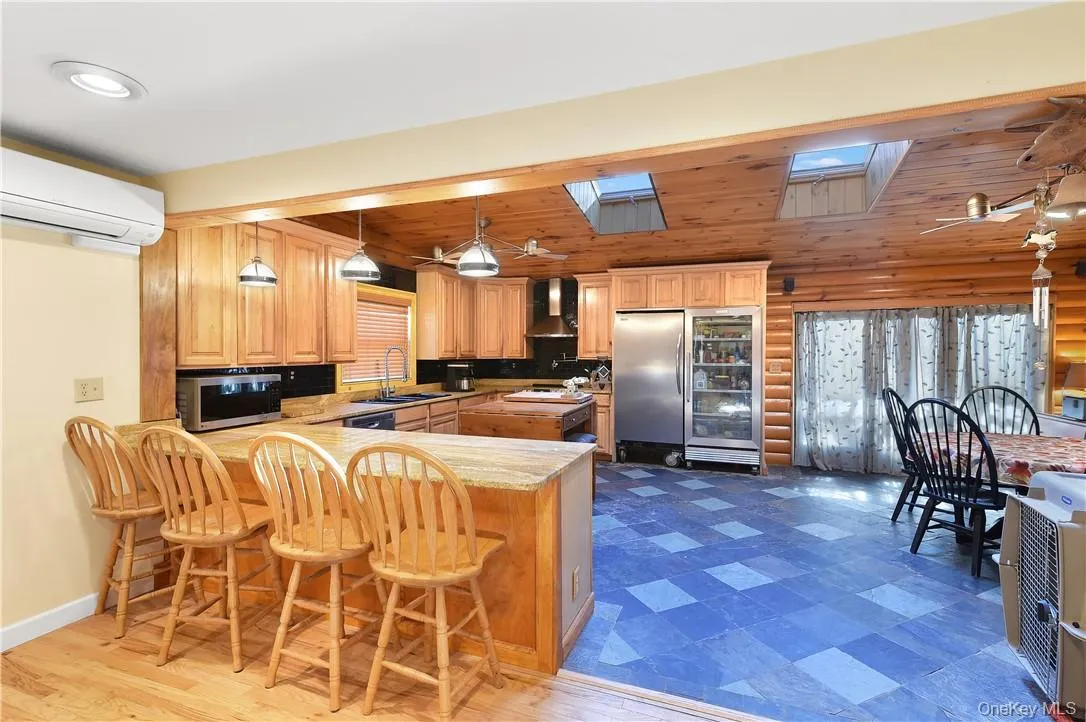 Kitchen featuring wall chimney range hood, wood ceiling, kitchen peninsula, a breakfast bar, and a skylight Kitchen featuring wall chimney range hood, wood ceiling, kitchen peninsula, a breakfast bar, and a skylight