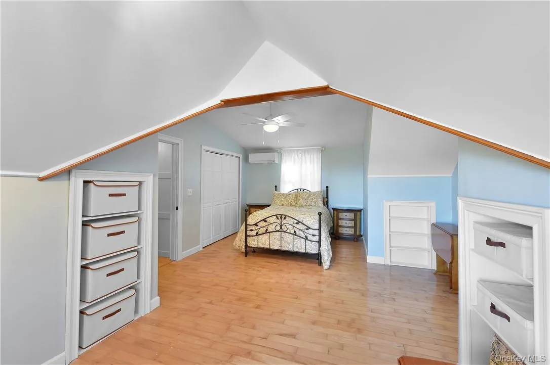 Bedroom featuring a wall unit AC, light hardwood / wood-style flooring, and lofted ceiling Bedroom featuring a wall unit AC, light hardwood / wood-style flooring, and lofted ceiling