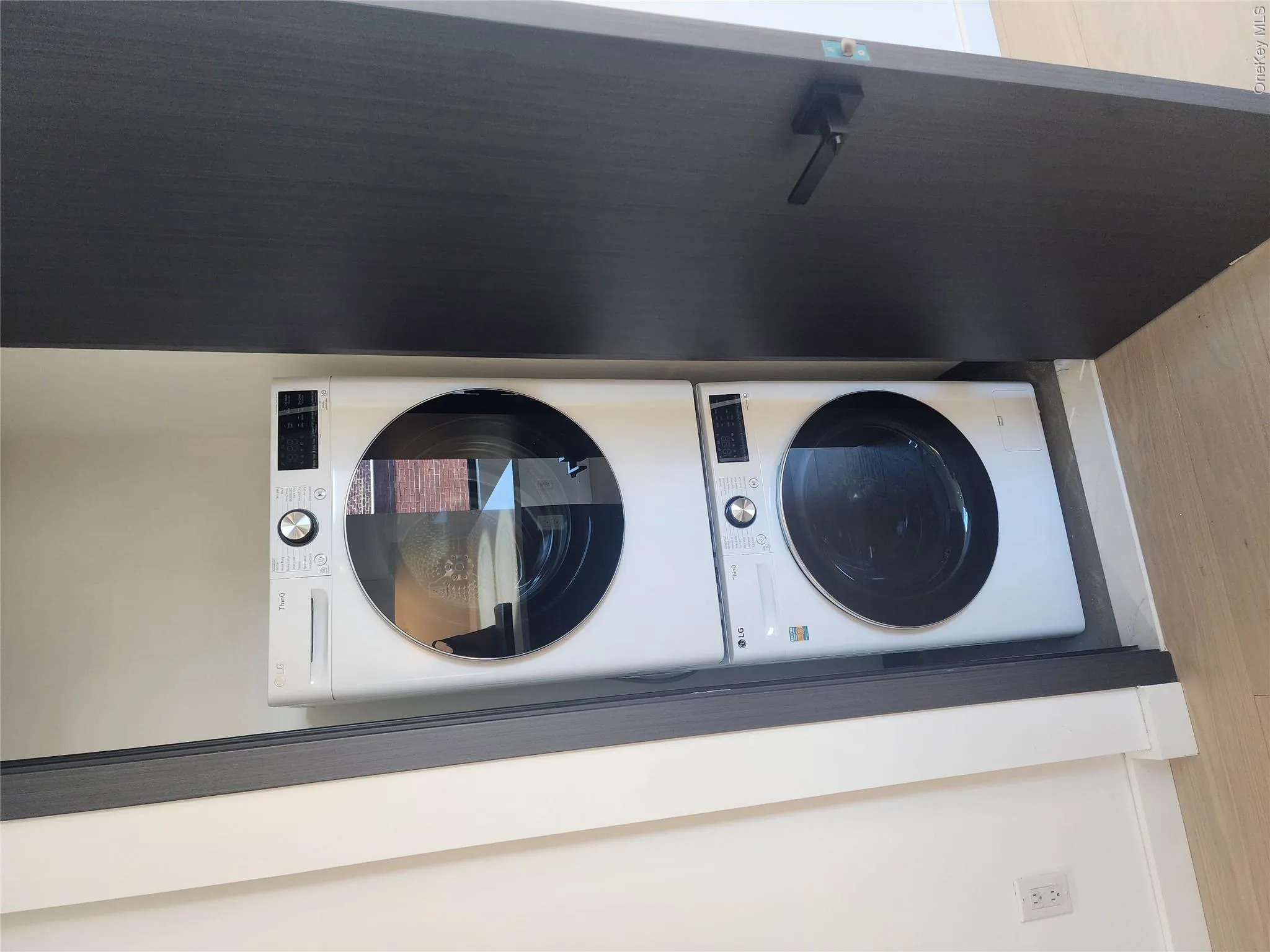 Stackable washer and dryer appliances within a dedicated closet, featuring a dark wood-finish door and contemporary hardware Stackable washer and dryer appliances within a dedicated closet, featuring a dark wood-finish door and contemporary hardware