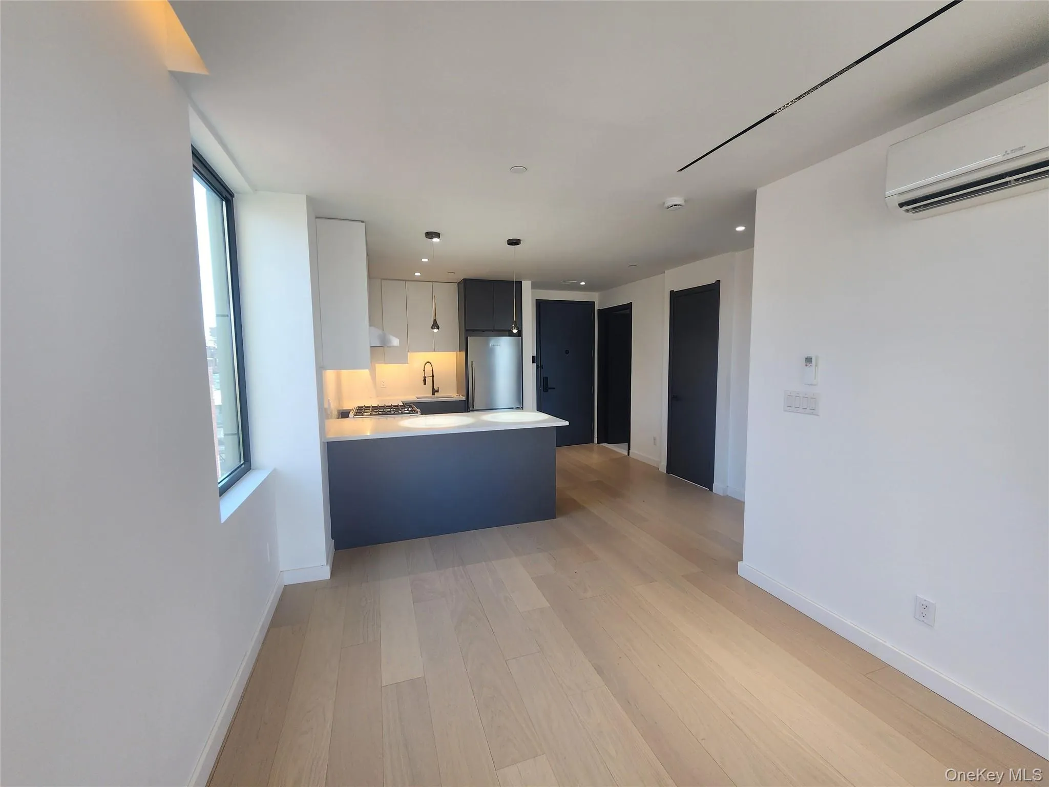Wood-finish flooring throughout, complemented by a modern kitchen featuring white and dark blue cabinetry, integrated appliances, and pendant lighting Wood-finish flooring throughout, complemented by a modern kitchen featuring white and dark blue cabinetry, integrated appliances, and pendant lighting