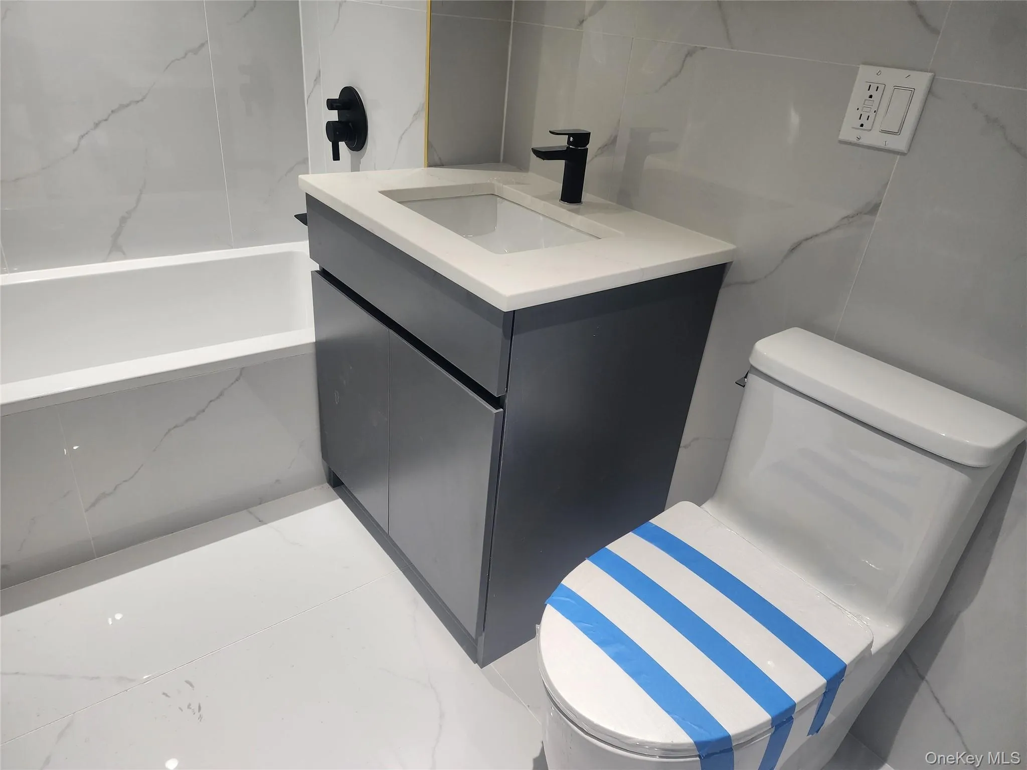 Bathroom featuring a white soaking tub, vanity with a rectangular basin, black faucet, and tiled walls Bathroom featuring a white soaking tub, vanity with a rectangular basin, black faucet, and tiled walls