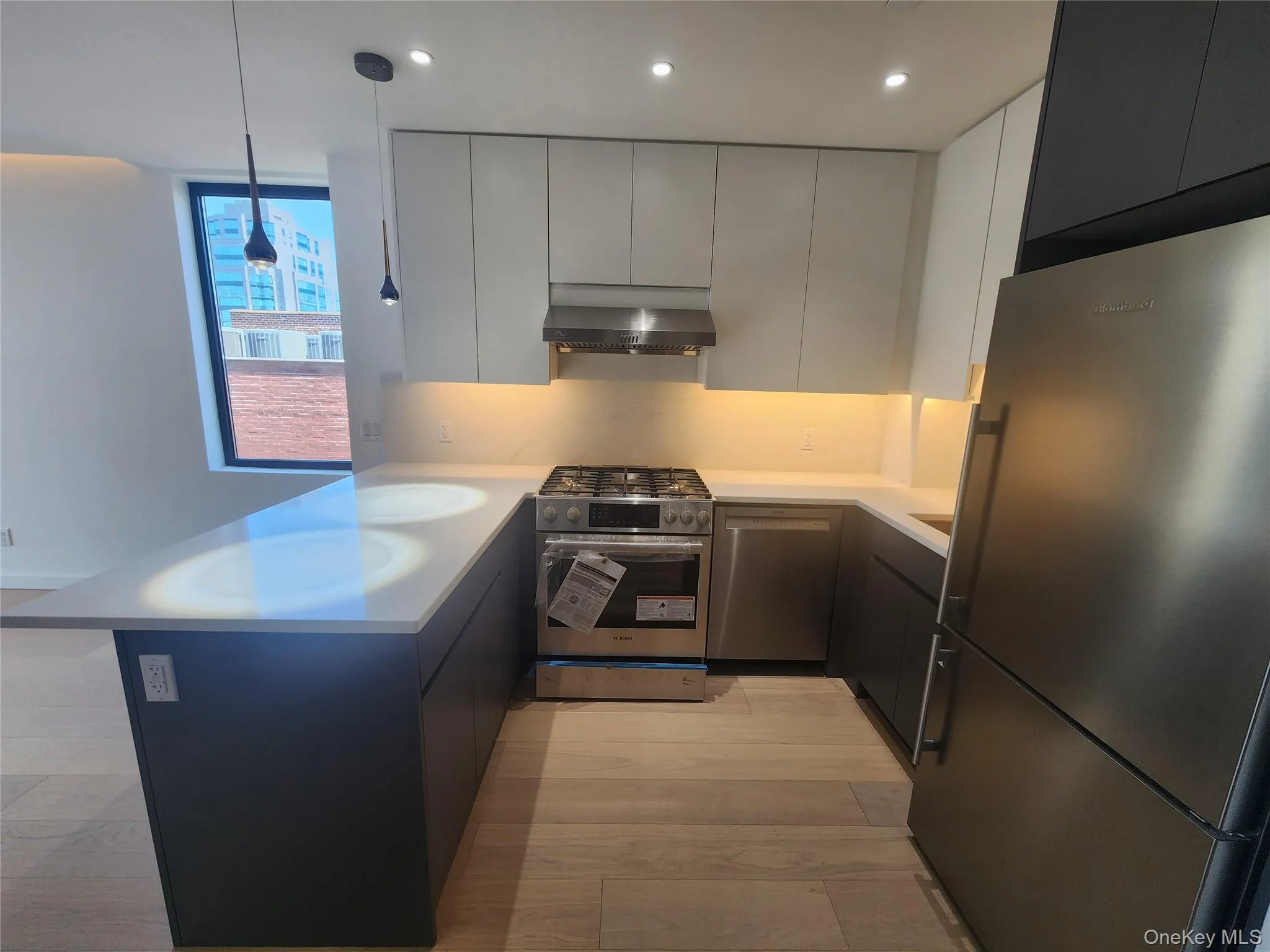 U-shaped kitchen featuring wood-finish flooring, stainless steel appliances, white countertops, dark lower cabinetry, and light upper cabinetry U-shaped kitchen featuring wood-finish flooring, stainless steel appliances, white countertops, dark lower cabinetry, and light upper cabinetry