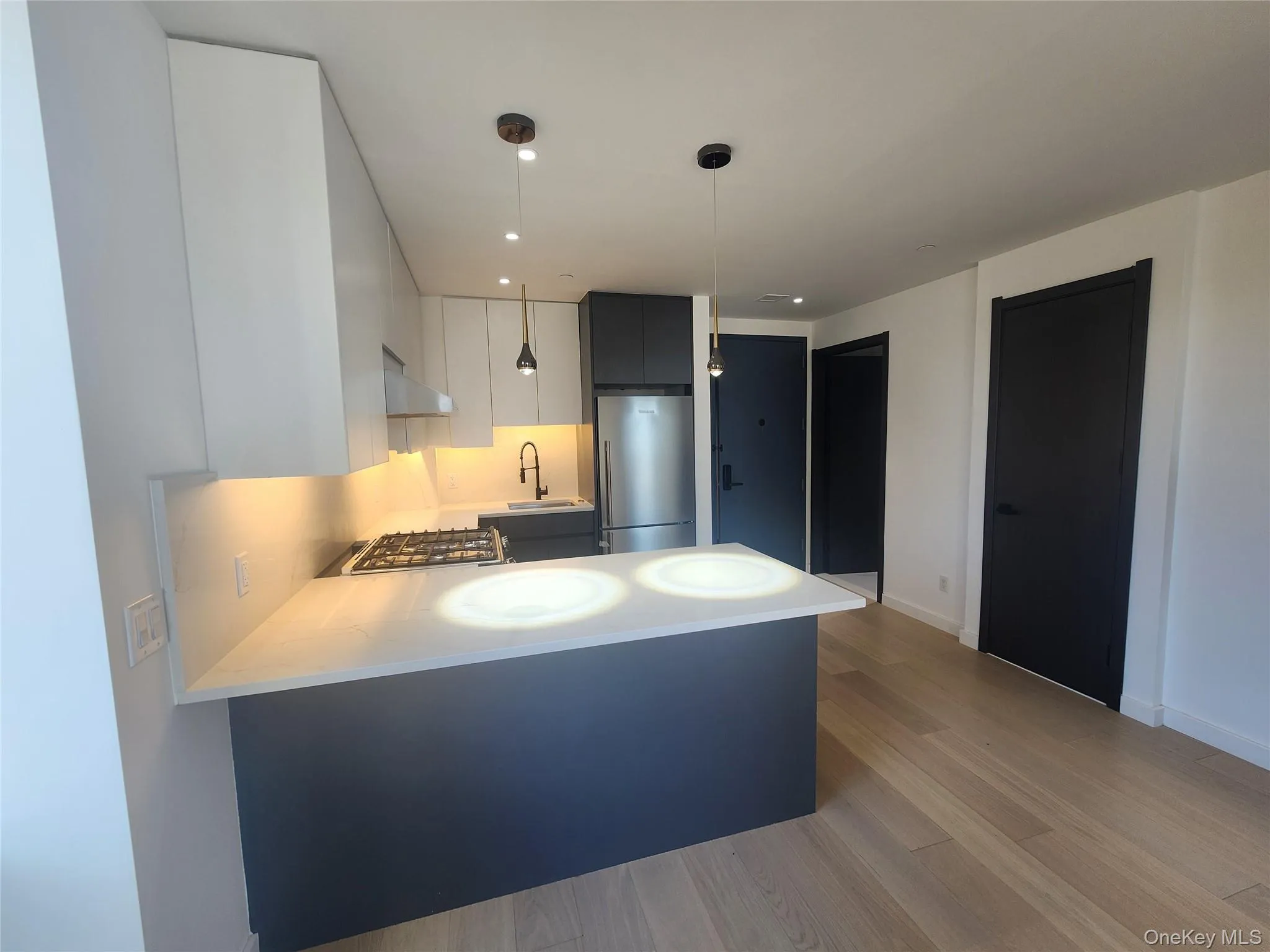 Modern kitchen featuring light-toned wood-finish flooring, white and gray cabinetry, a gas cooktop, and stainless steel appliances Modern kitchen featuring light-toned wood-finish flooring, white and gray cabinetry, a gas cooktop, and stainless steel appliances