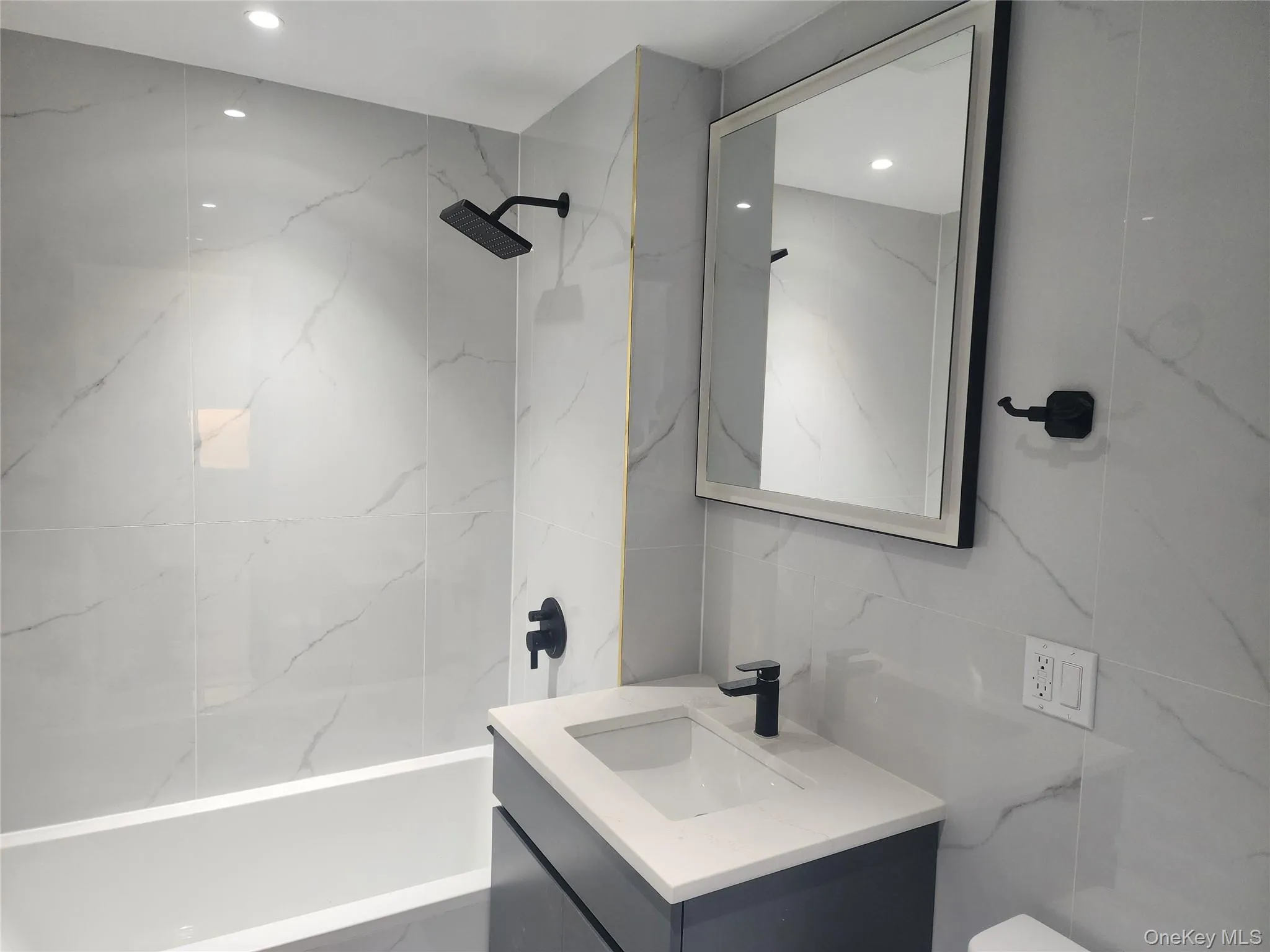 Full-height tiled walls, recessed lighting, matte black fixtures, integrated bathtub, and a floating vanity with a vessel sink Full-height tiled walls, recessed lighting, matte black fixtures, integrated bathtub, and a floating vanity with a vessel sink