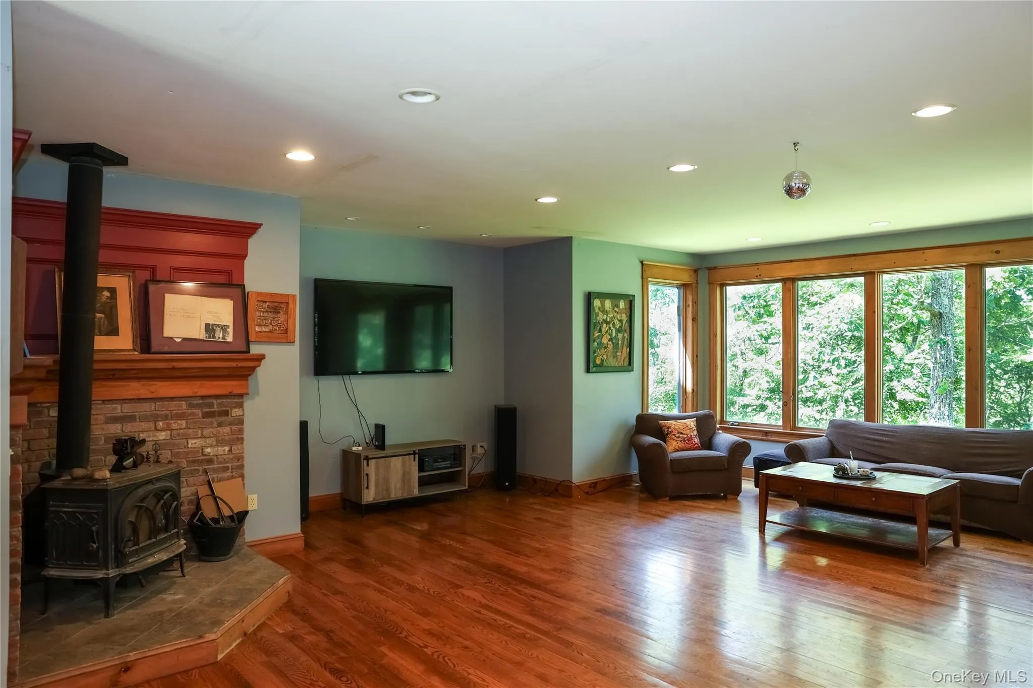 Hardwood flooring, recessed ceiling lighting, a wood-burning stove with a brick and stone surround, and extensive window framing Hardwood flooring, recessed ceiling lighting, a wood-burning stove with a brick and stone surround, and extensive window framing