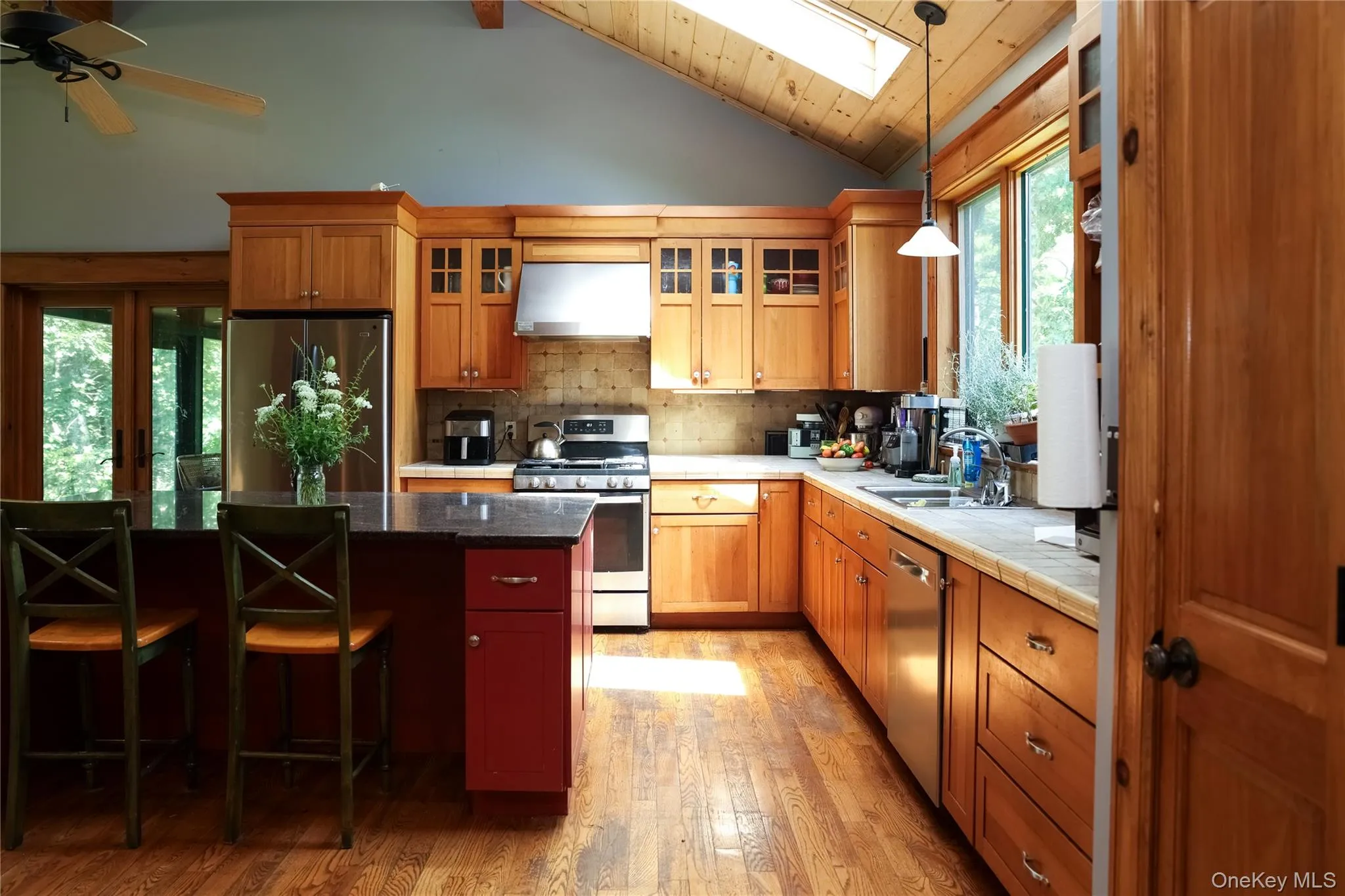 Kitchen featuring a vaulted wood-paneled ceiling with skylight, wood-finish flooring, wood cabinetry, and an island with a contrasting base Kitchen featuring a vaulted wood-paneled ceiling with skylight, wood-finish flooring, wood cabinetry, and an island with a contrasting base