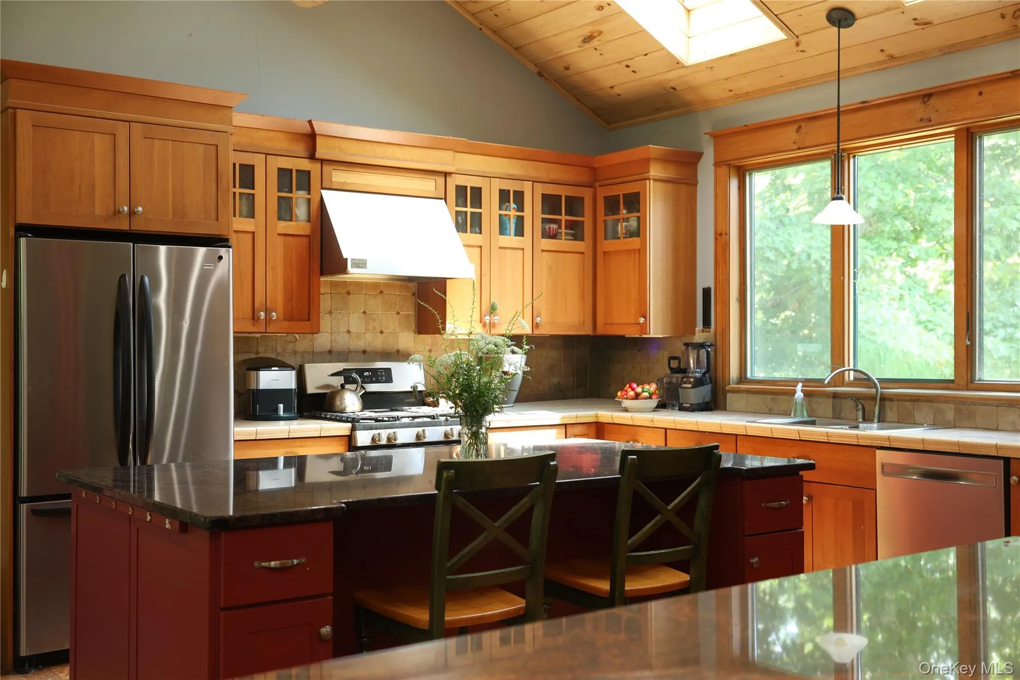 Kitchen featuring wood cabinetry, stainless steel appliances, a center island with a dark countertop, a vaulted wood-paneled ceiling, and a skylight Kitchen featuring wood cabinetry, stainless steel appliances, a center island with a dark countertop, a vaulted wood-paneled ceiling, and a skylight