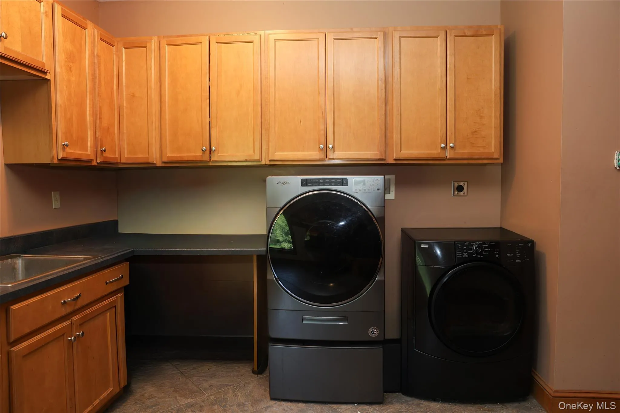 Utility area with wood-finish cabinetry, a utility sink, dark countertop, and tile flooring Utility area with wood-finish cabinetry, a utility sink, dark countertop, and tile flooring