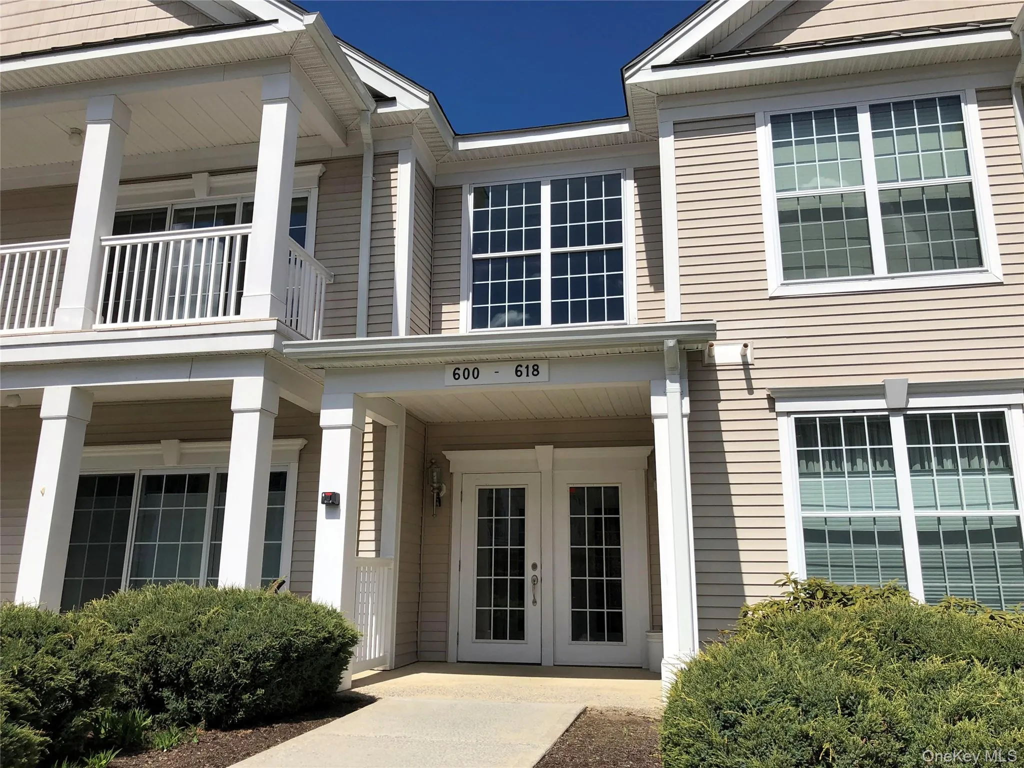 Entryway featuring double French doors, a covered porch with white columns, and upper-level balconies with white railings Entryway featuring double French doors, a covered porch with white columns, and upper-level balconies with white railings