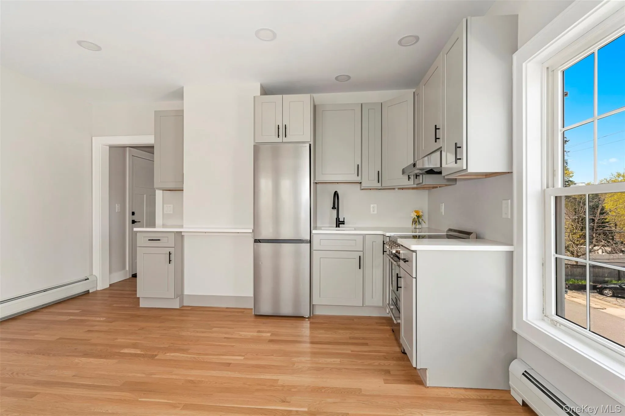 Kitchen with light wood-style flooring, a sink, baseboard heating, light countertops, and appliances with stainless steel finishes Kitchen with light wood-style flooring, a sink, baseboard heating, light countertops, and appliances with stainless steel finishes