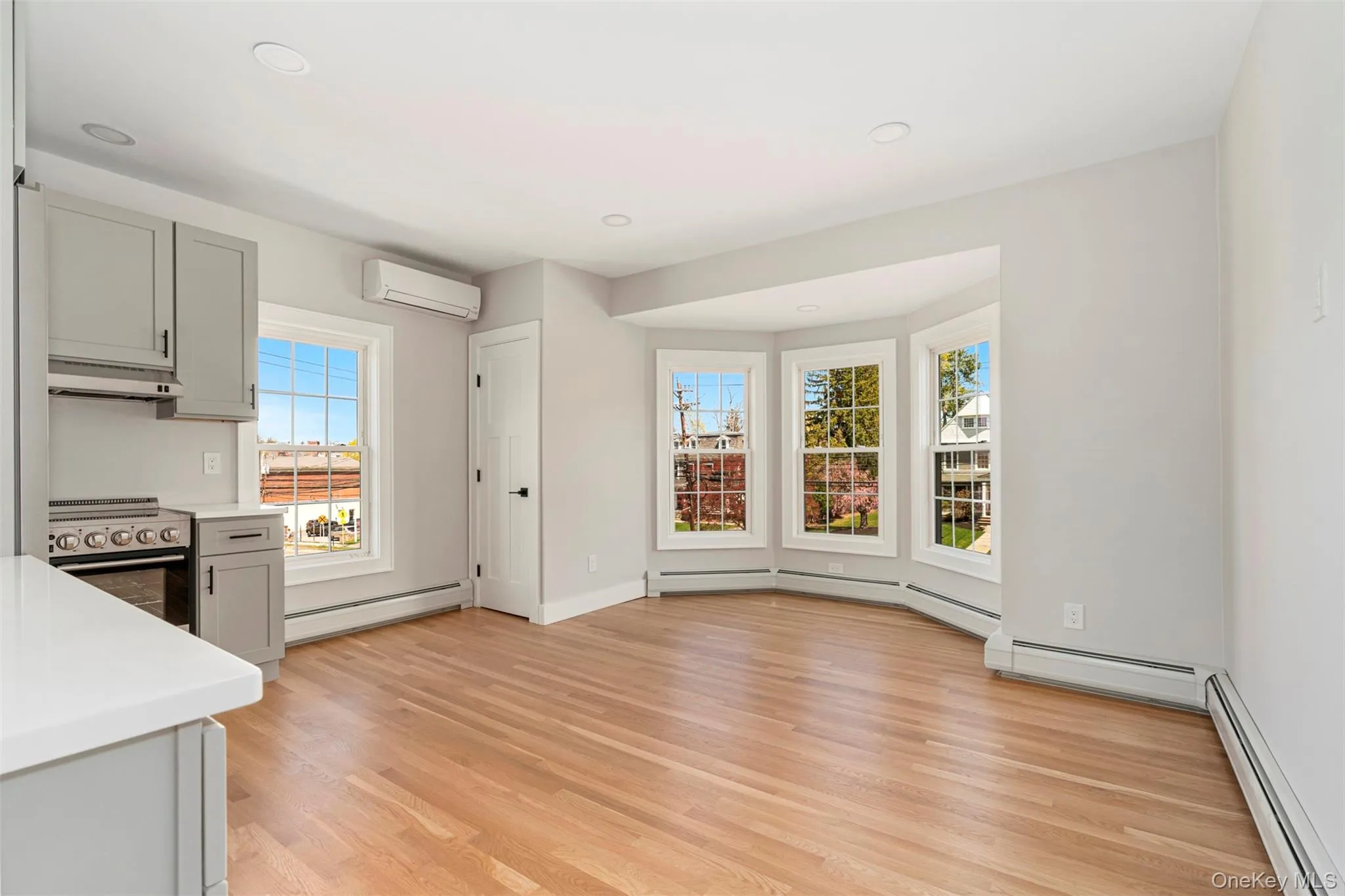 Kitchen featuring an AC wall unit, gray cabinetry, stainless steel electric range oven, and a baseboard radiator Kitchen featuring an AC wall unit, gray cabinetry, stainless steel electric range oven, and a baseboard radiator
