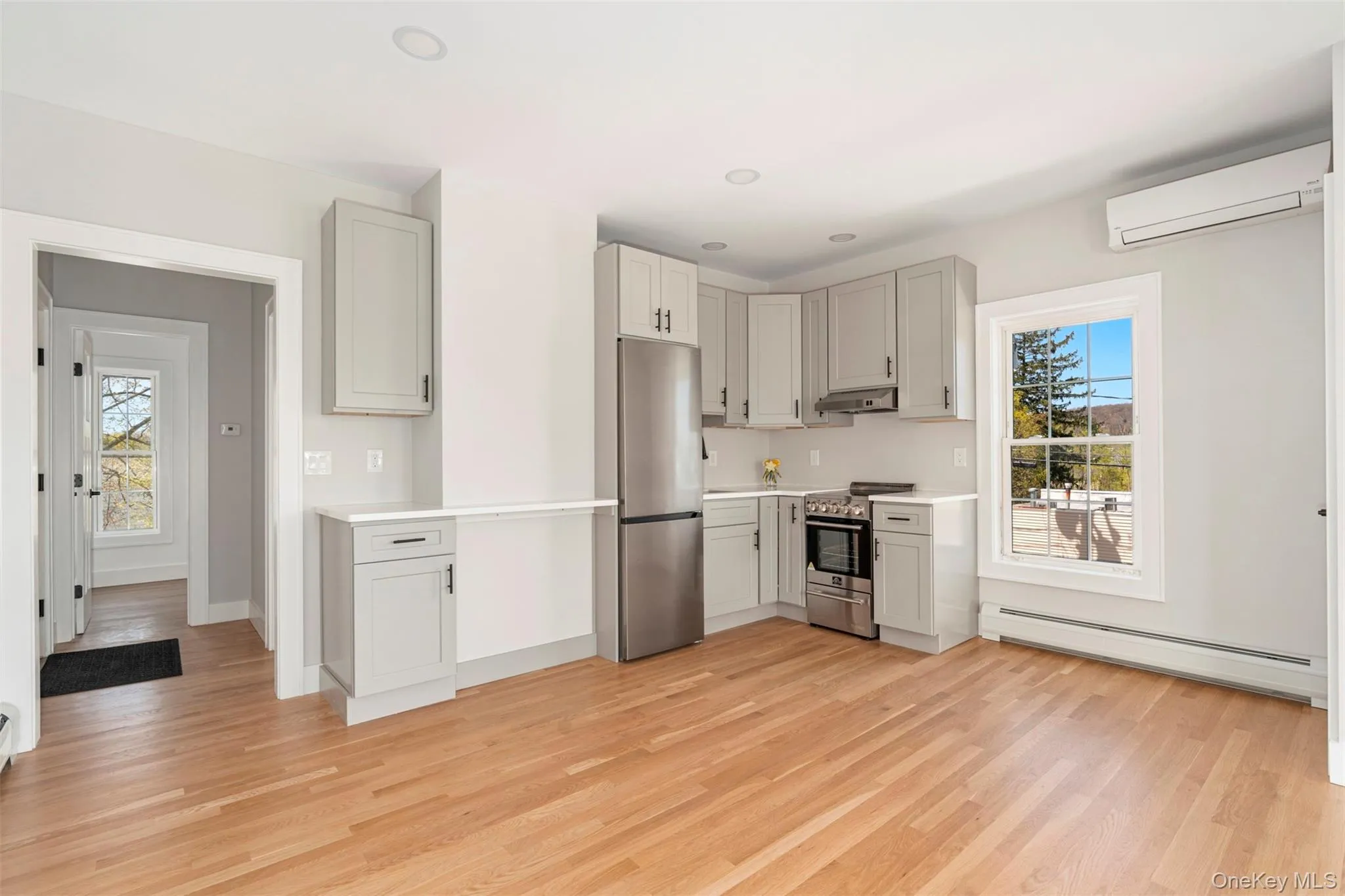 Kitchen featuring light wood finished floors, stainless steel appliances, an AC wall unit, baseboard heating, and under cabinet range hood Kitchen featuring light wood finished floors, stainless steel appliances, an AC wall unit, baseboard heating, and under cabinet range hood