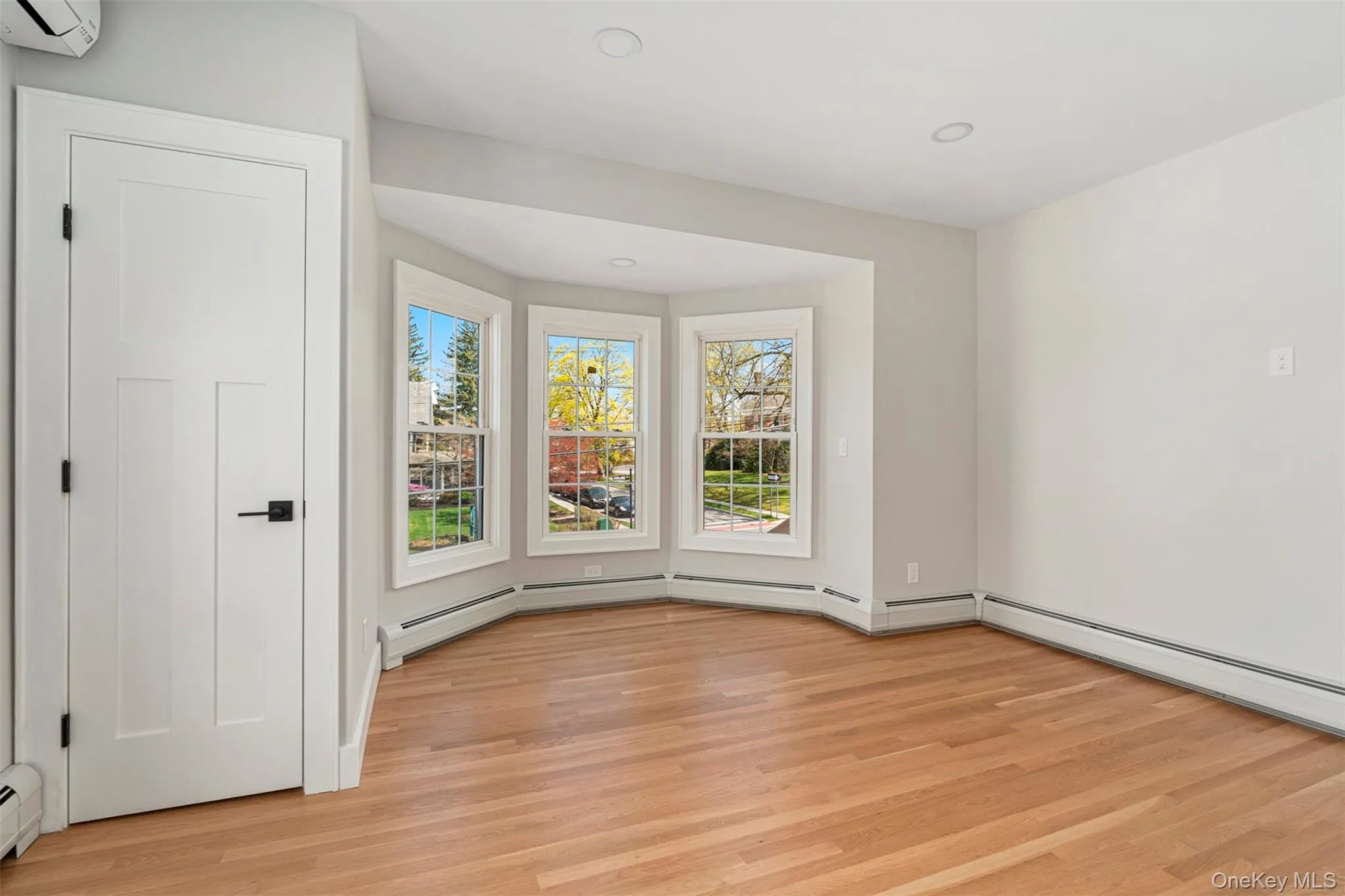 Empty room with a baseboard heating unit, a wall mounted air conditioner, a wealth of natural light, and light wood finished floors Empty room with a baseboard heating unit, a wall mounted air conditioner, a wealth of natural light, and light wood finished floors