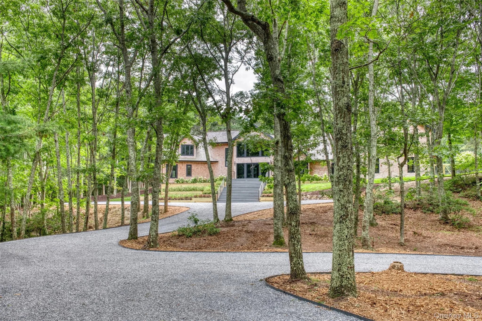 Wooded property with a gravel driveway, mature trees, and a multi-level home featuring gables and wood siding Wooded property with a gravel driveway, mature trees, and a multi-level home featuring gables and wood siding