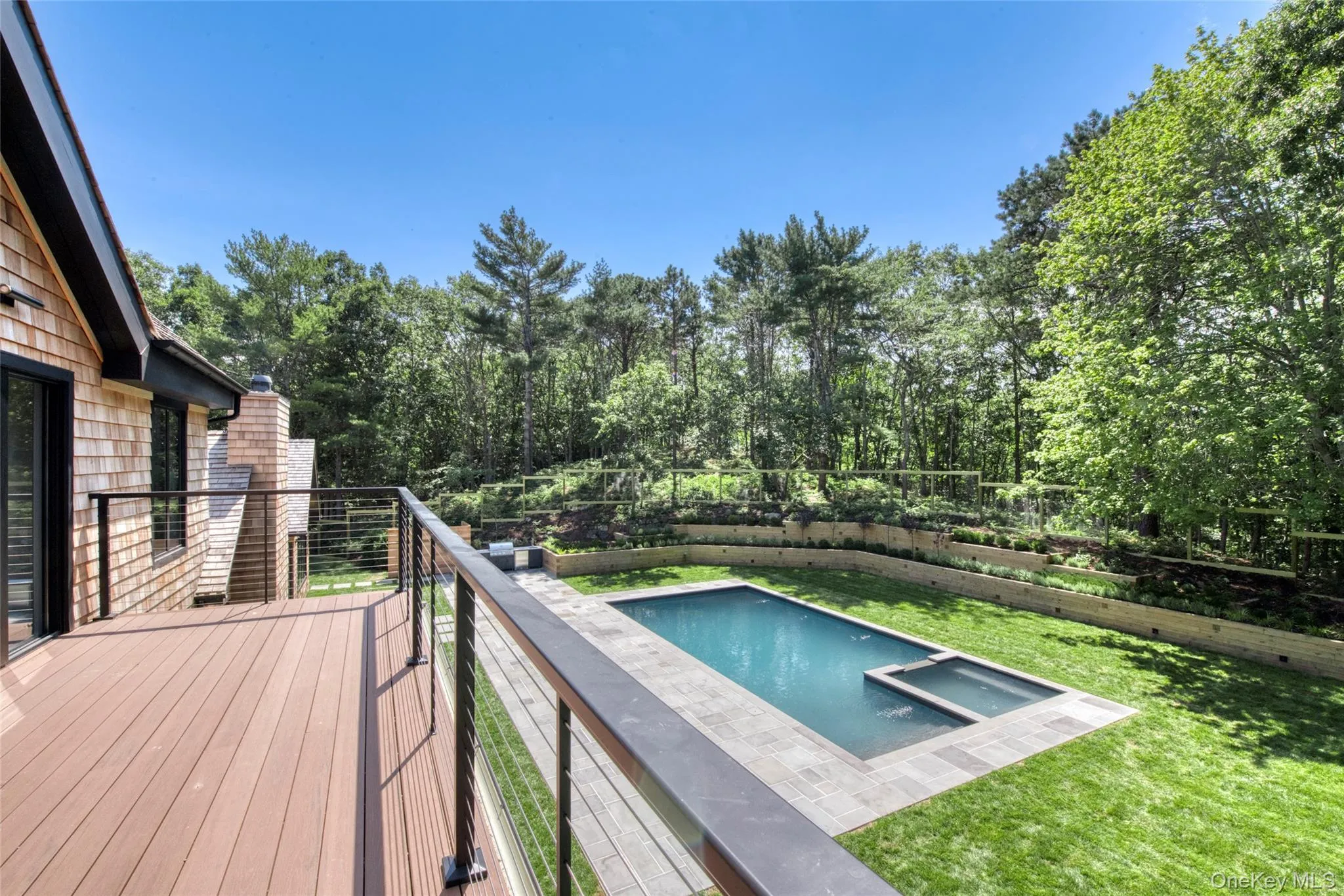 Expansive deck with cable railing, shingle siding, rectangular swimming pool, integrated spa, and tiered landscaping Expansive deck with cable railing, shingle siding, rectangular swimming pool, integrated spa, and tiered landscaping