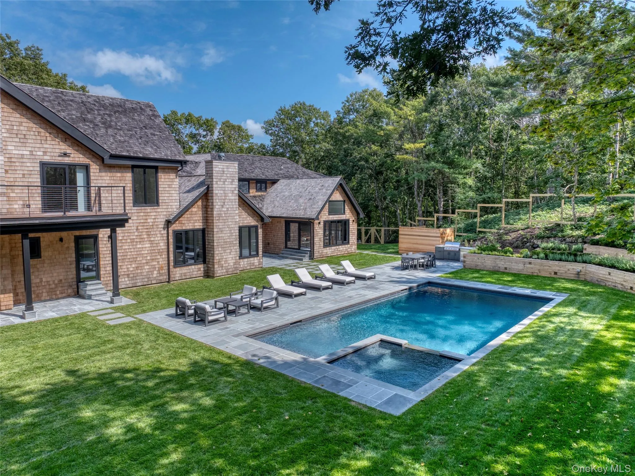 Shingle-sided exterior with a natural stone patio and a rectangular swimming pool with an integrated spa
