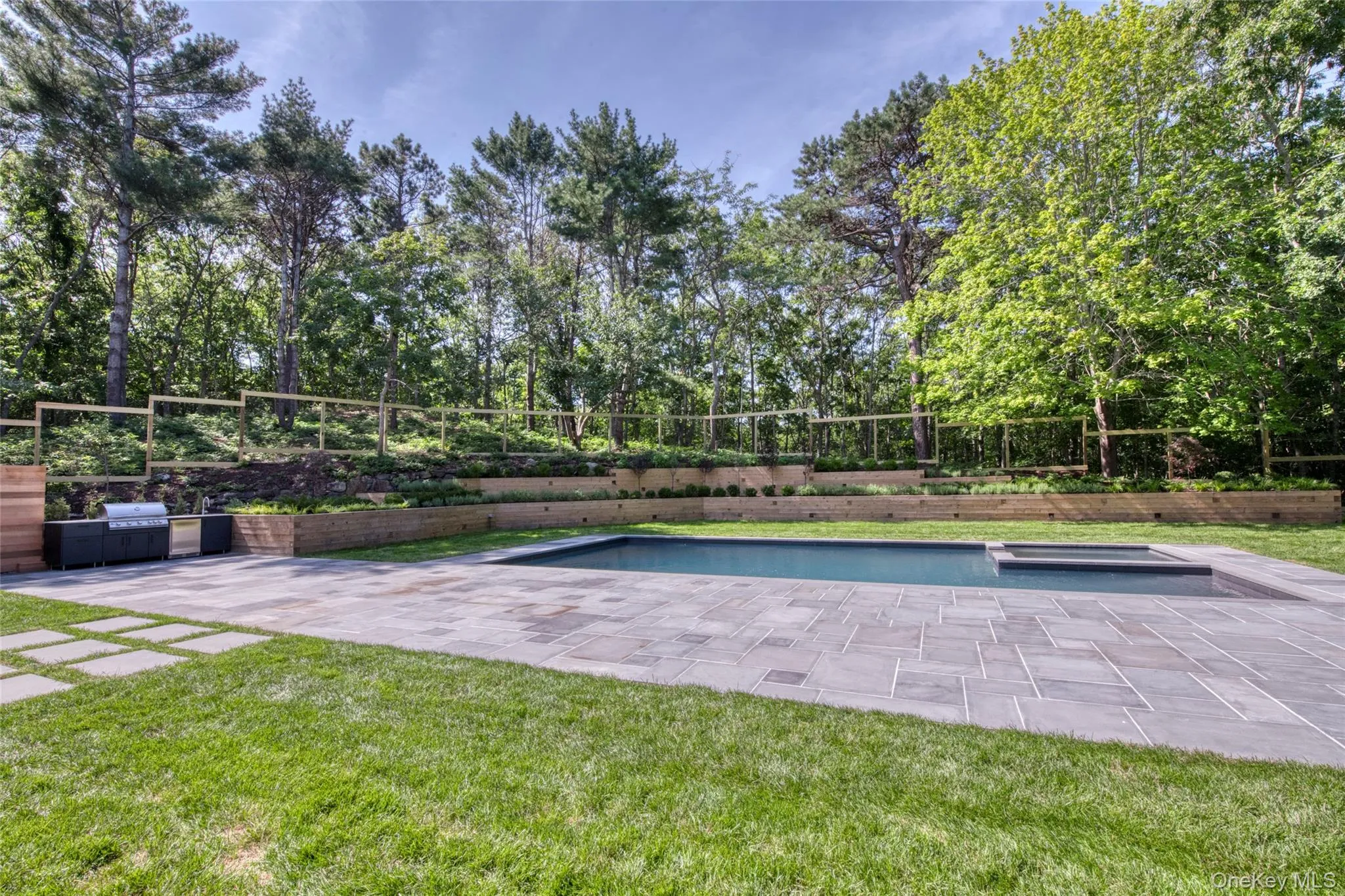 Expansive backyard featuring a rectangular swimming pool, integrated spa, and a built-in outdoor kitchen with grill Expansive backyard featuring a rectangular swimming pool, integrated spa, and a built-in outdoor kitchen with grill